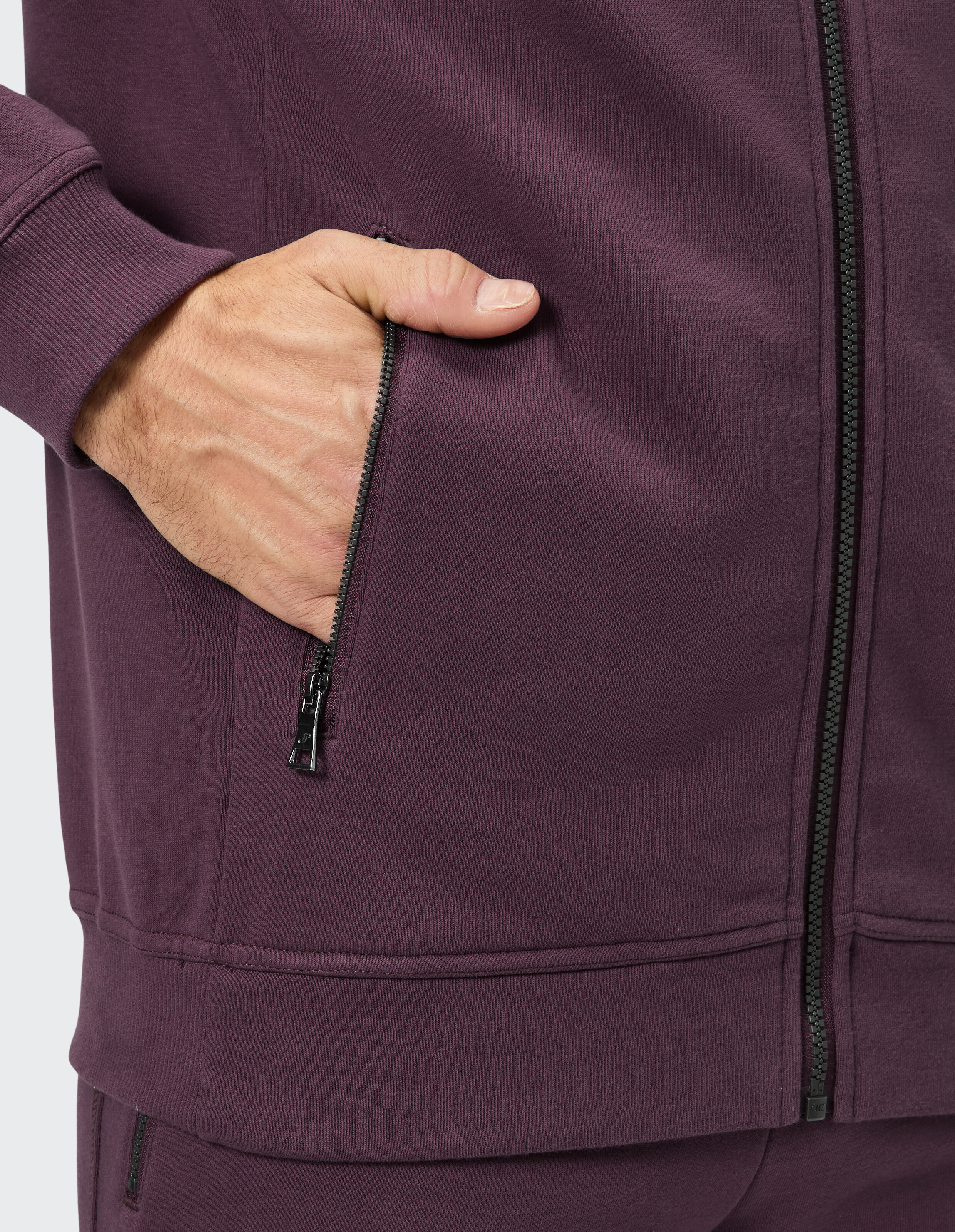 Nahaufnahme einer Hand in der Tasche einer lila Reißverschlussjacke, die den lässigen Stil unterstreicht.