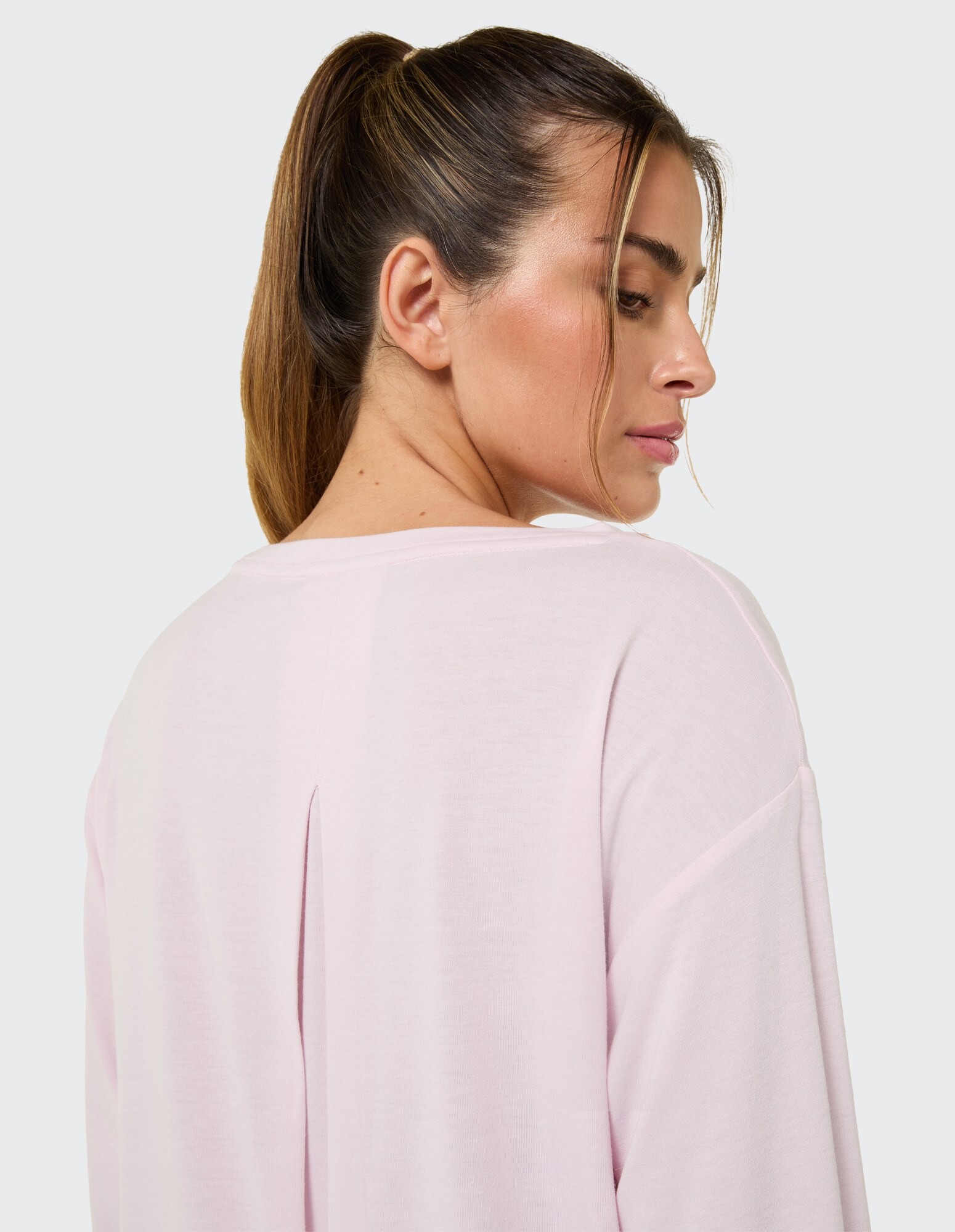 Rückansicht einer Frau in einem hellrosa Freizeittop mit stylischem Ausschnitt.