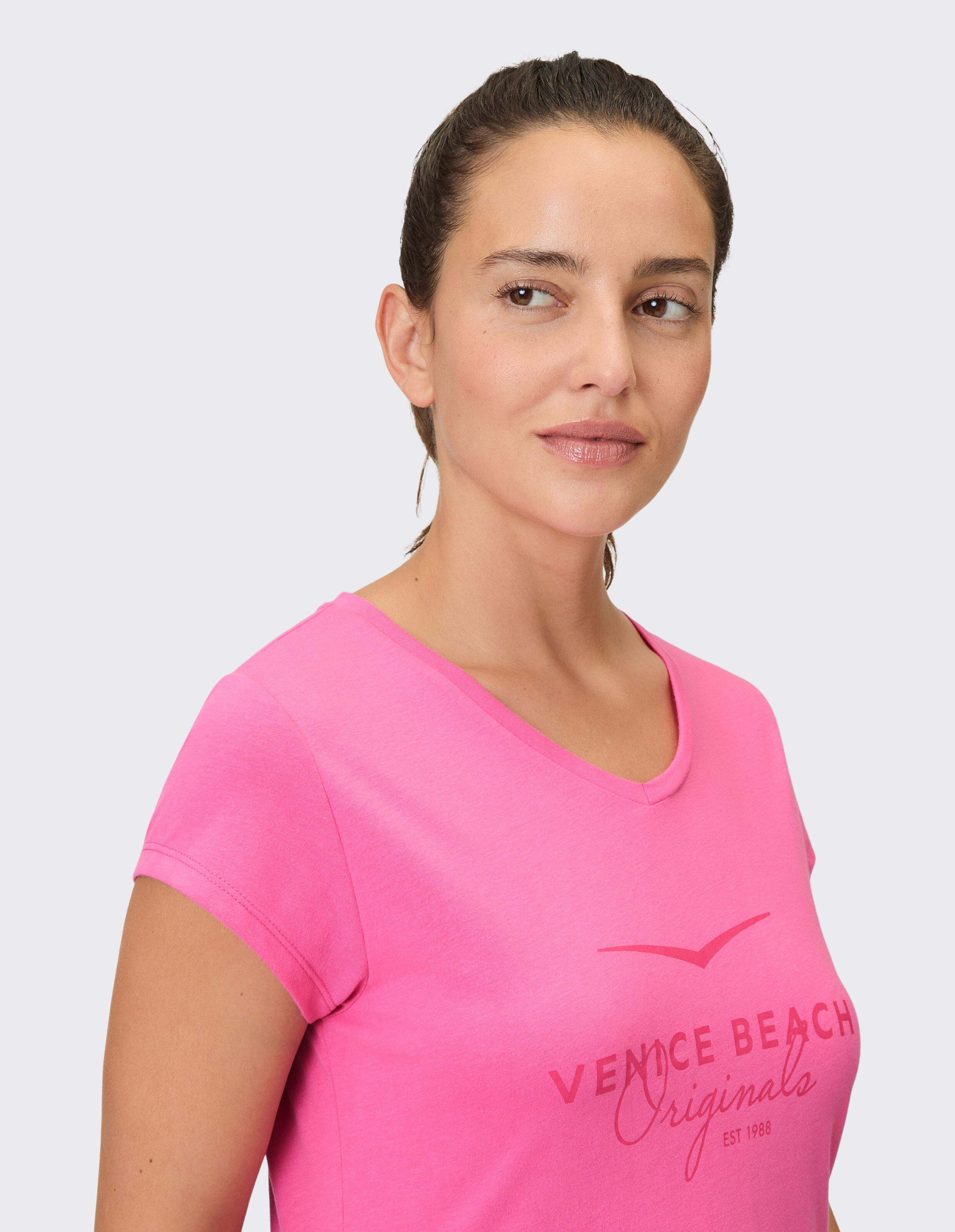 Frau trägt ein rosa lässiges T-Shirt mit V-Ausschnitt und Venice Beach-Logoaufdruck.