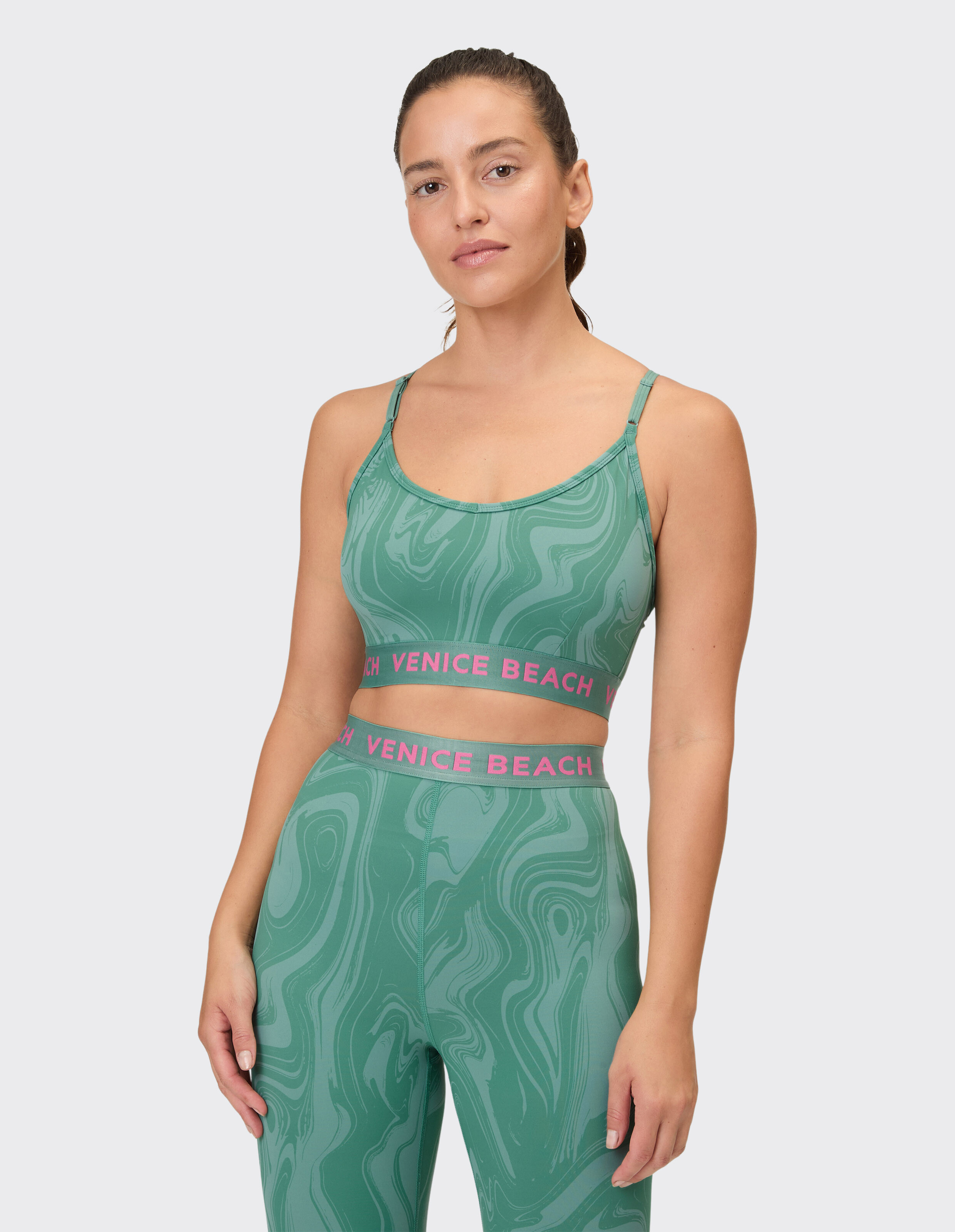 Frau trägt einen Sport-BH mit grünem Marmor-Print und Leggings von Venice Beach.