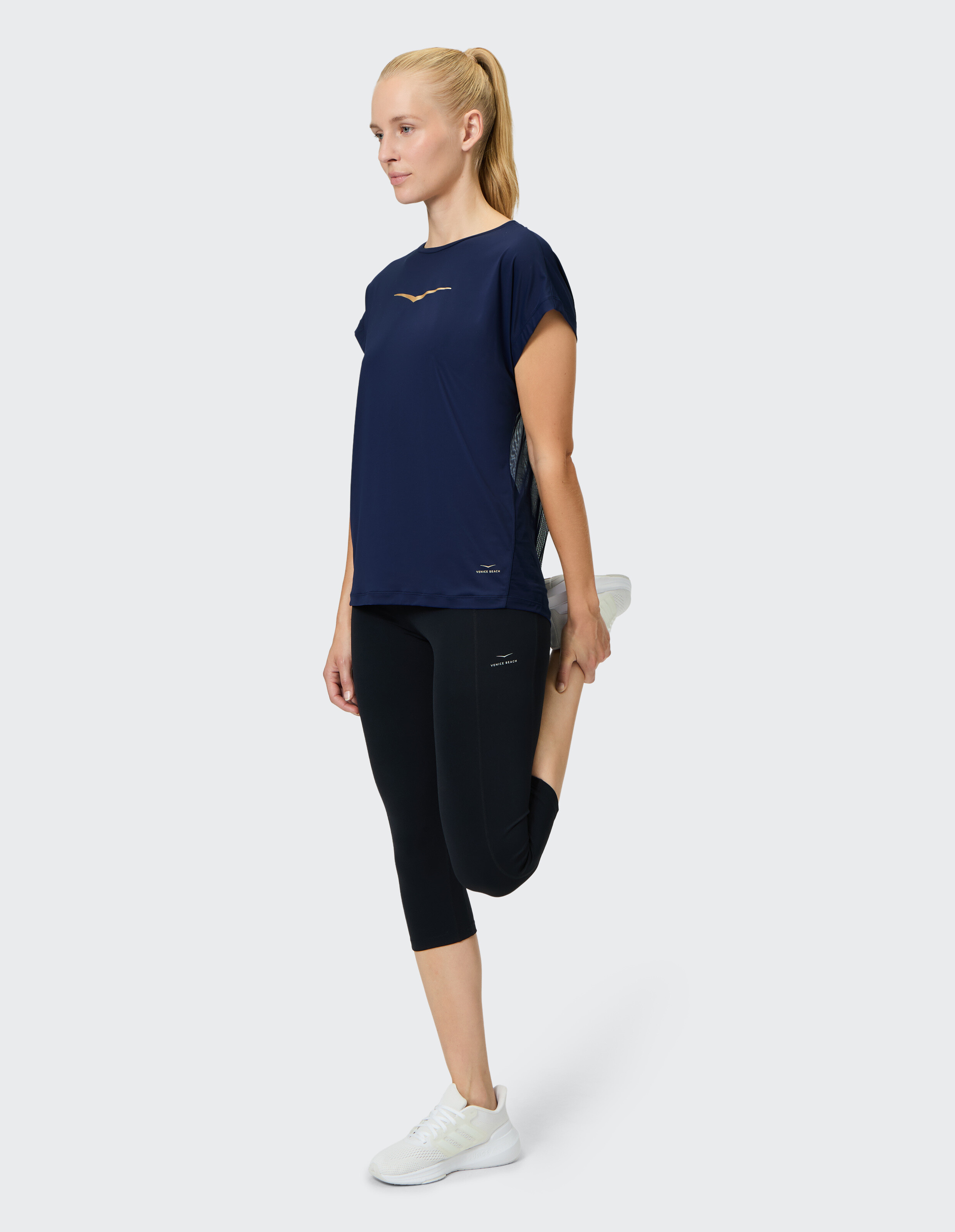 Frau beim Dehnen in einem dunkelblauen Sporttop und schwarzen Capri-Leggings, ideal für Freizeitkleidung.