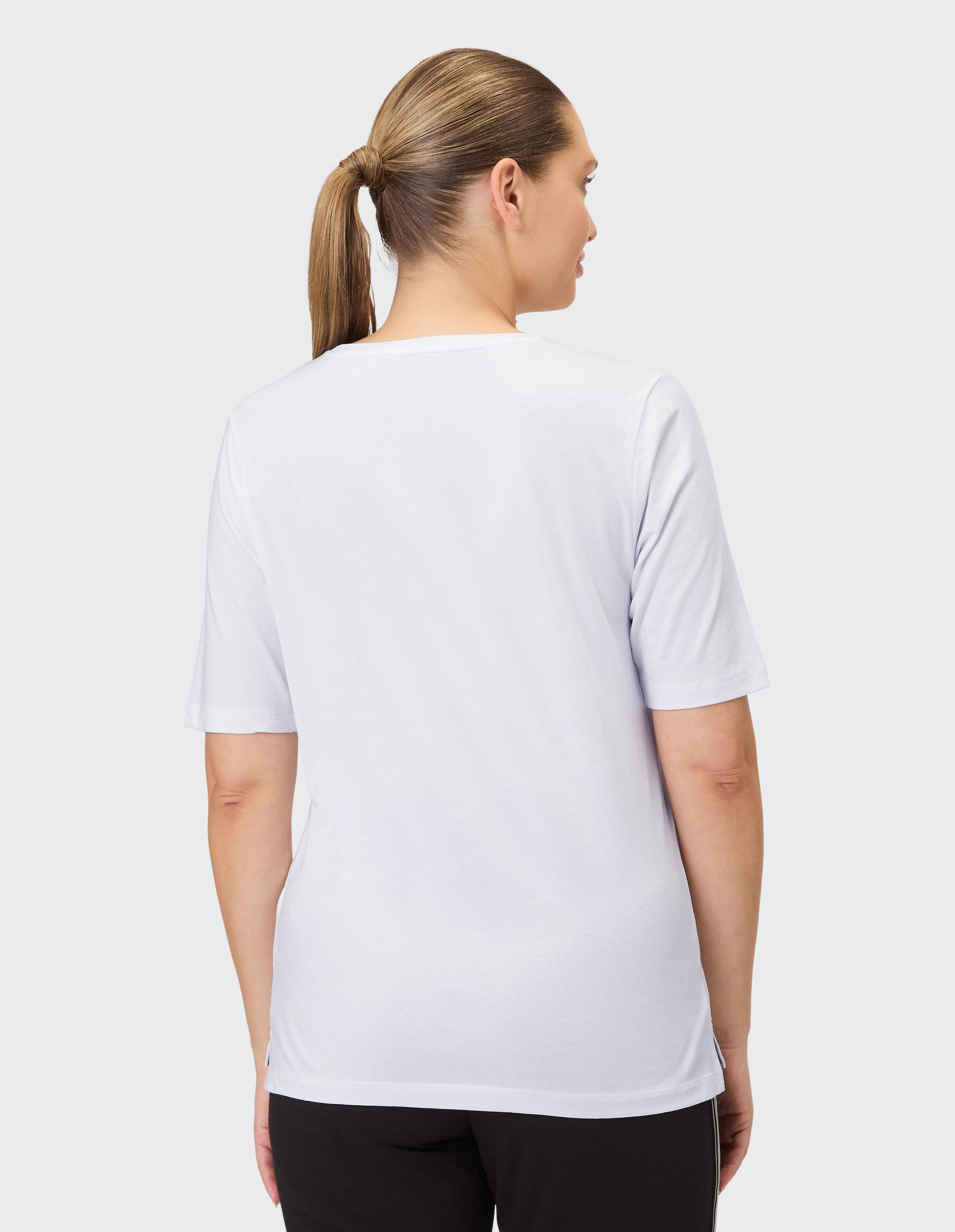 Rückansicht einer Frau, die ein weißes Freizeit-T-Shirt trägt, perfekt zum Entspannen.