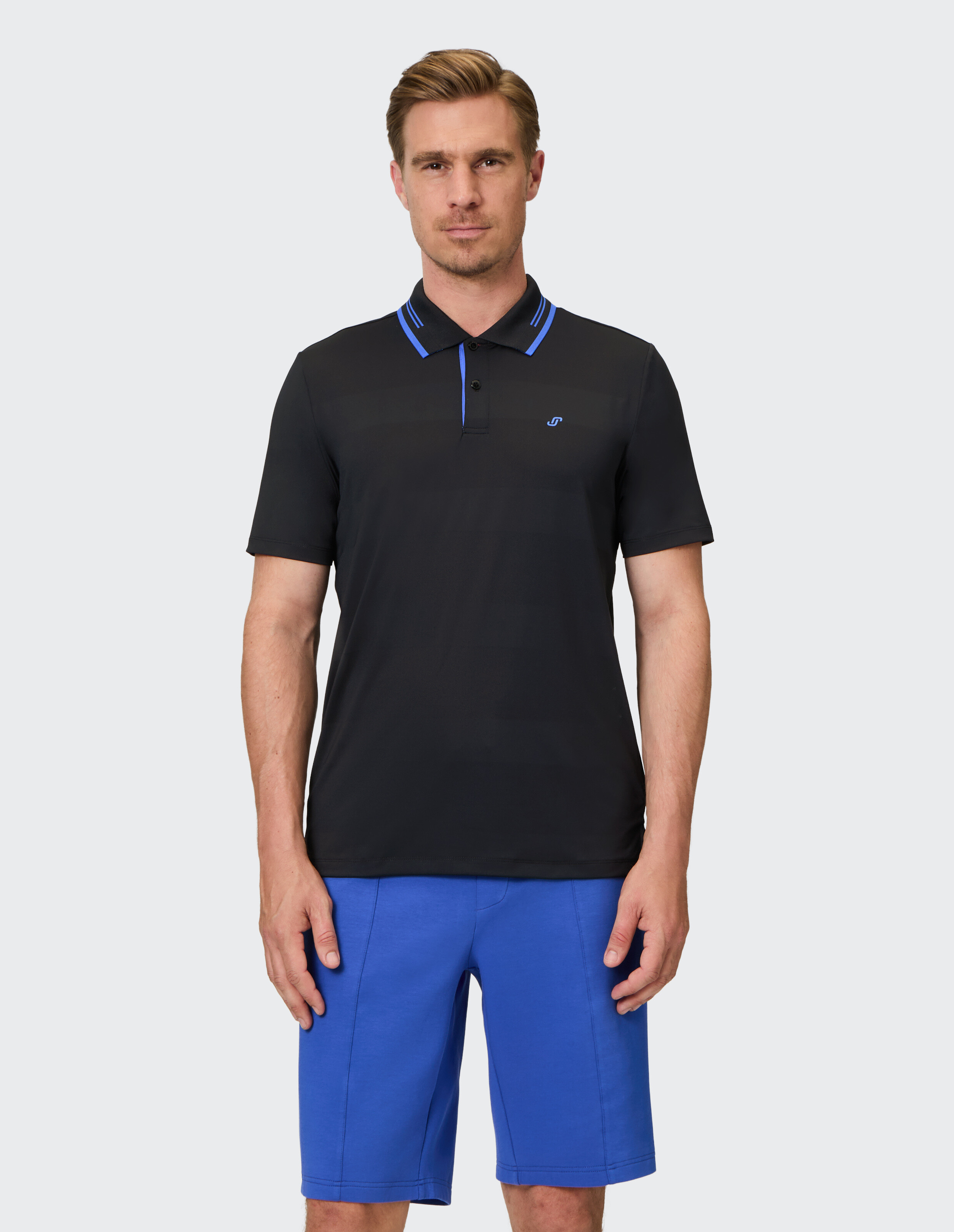 Mann trägt ein schwarzes Poloshirt mit blauen Akzenten und blauen Shorts im lässigen Stil.
