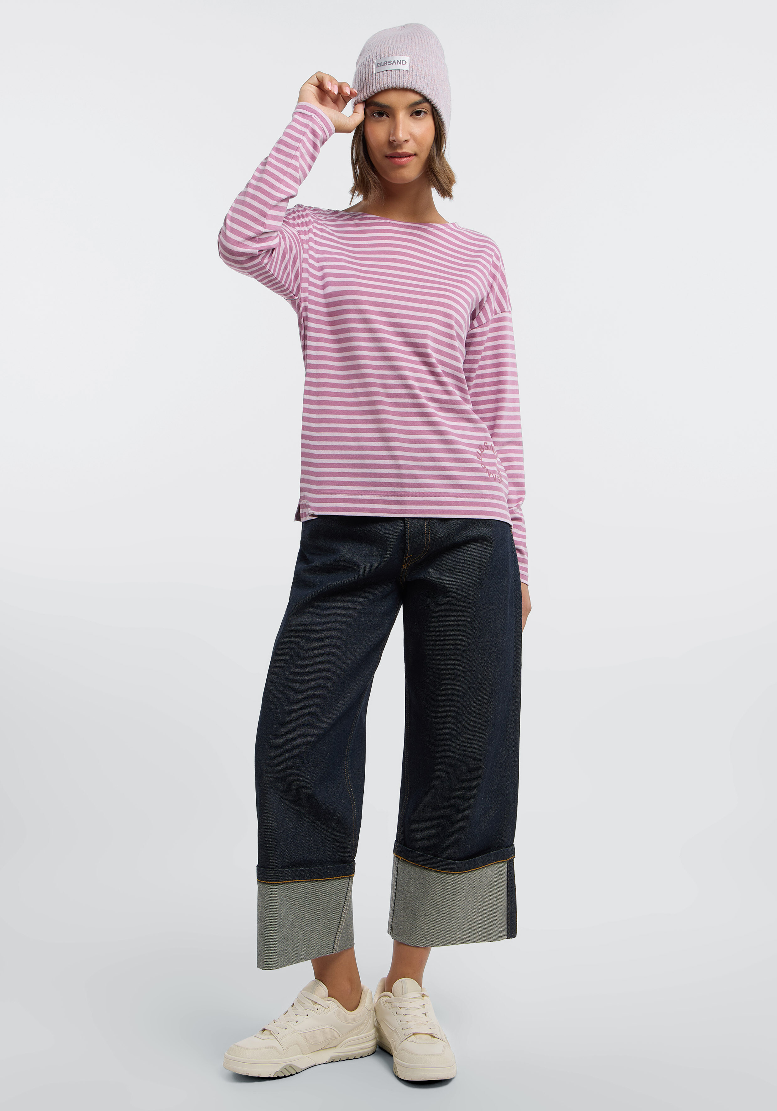 Frau trägt ein rosa gestreiftes Langarmhemd, eine Mütze und Jeans mit weitem Bein.