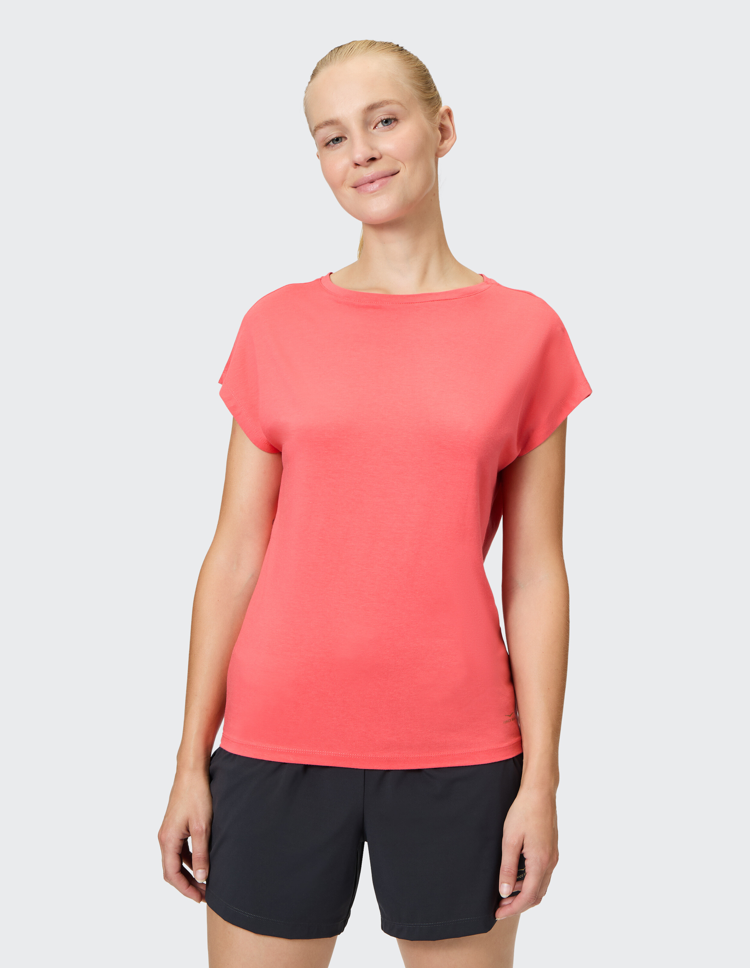 Frau trägt ein korallenrosa Freizeit-T-Shirt und dunkle Shorts für einen bequemen Lounge-Look.