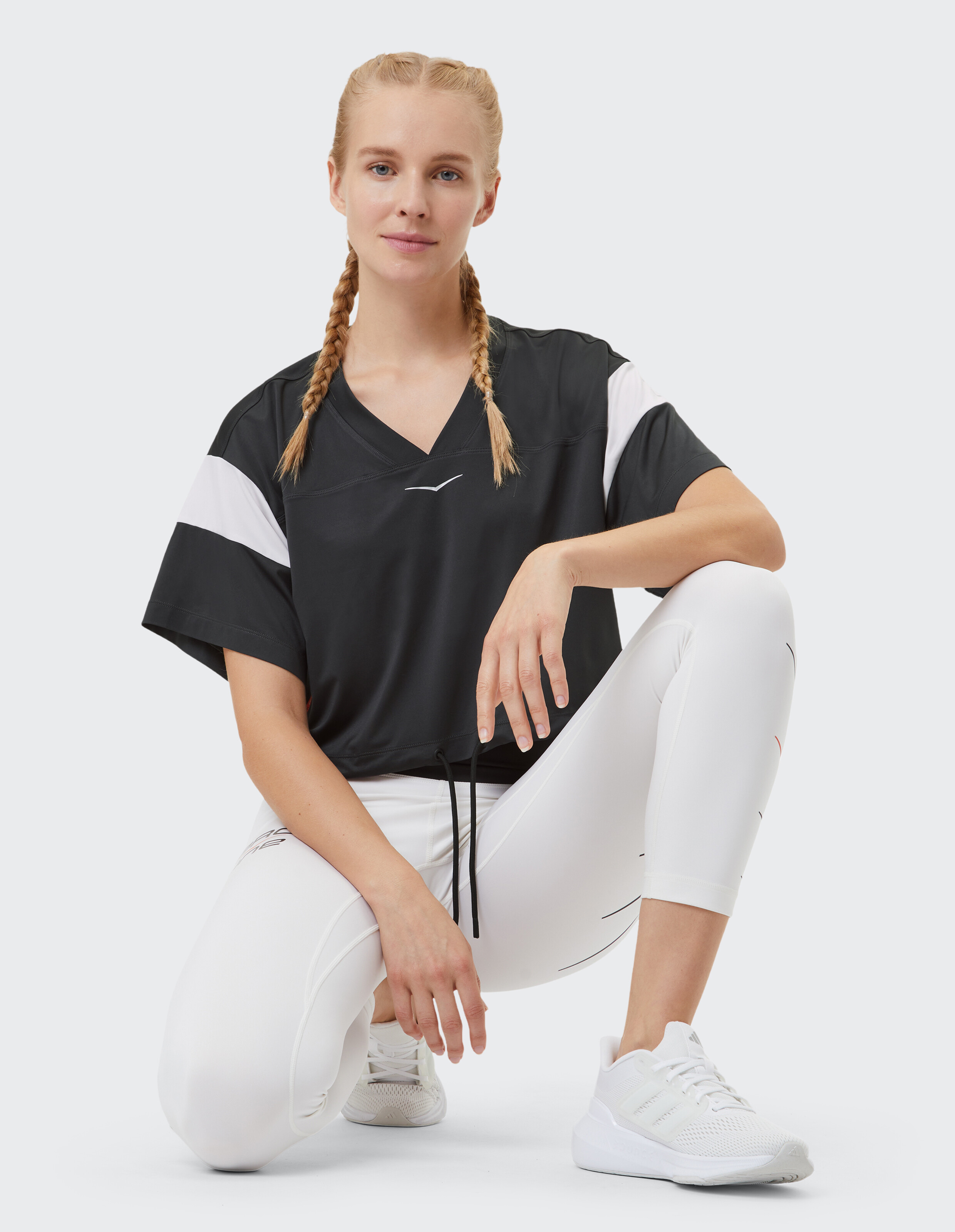Frau trägt ein schwarzes Top mit V-Ausschnitt und weiße Leggings, perfekt für einen lässigen, sportlichen Stil.