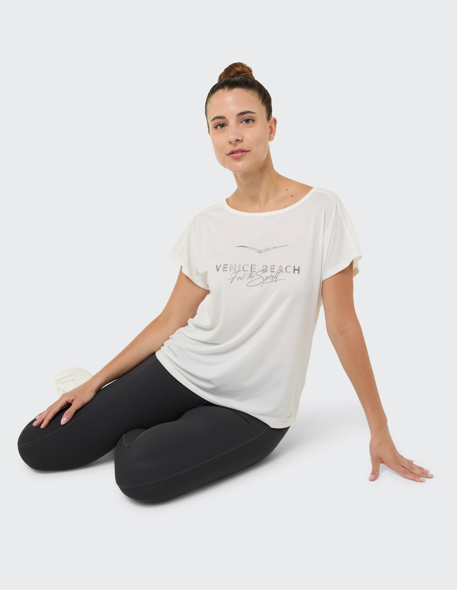 Frau in einem lässigen weißen T-Shirt mit „Venice Beach“-Aufdruck und schwarzen Leggings.