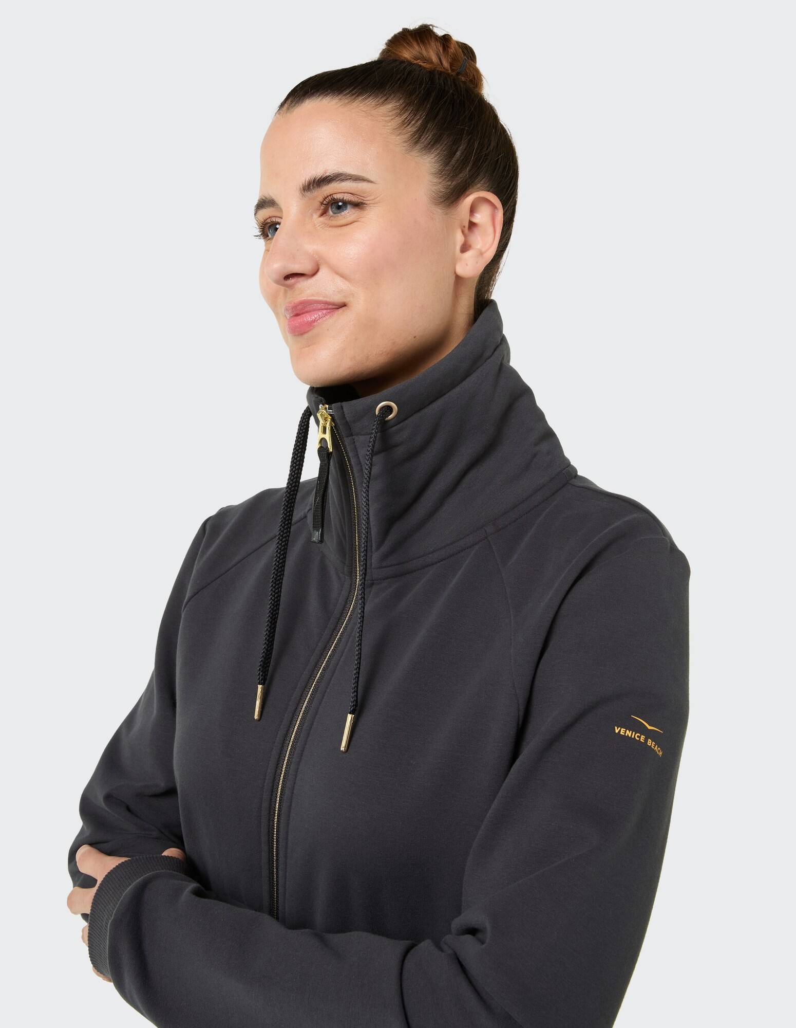 Stilvolle Frau in einem dunklen Kapuzenpullover mit Reißverschluss und goldenen Akzenten, perfekt für Freizeitkleidung.