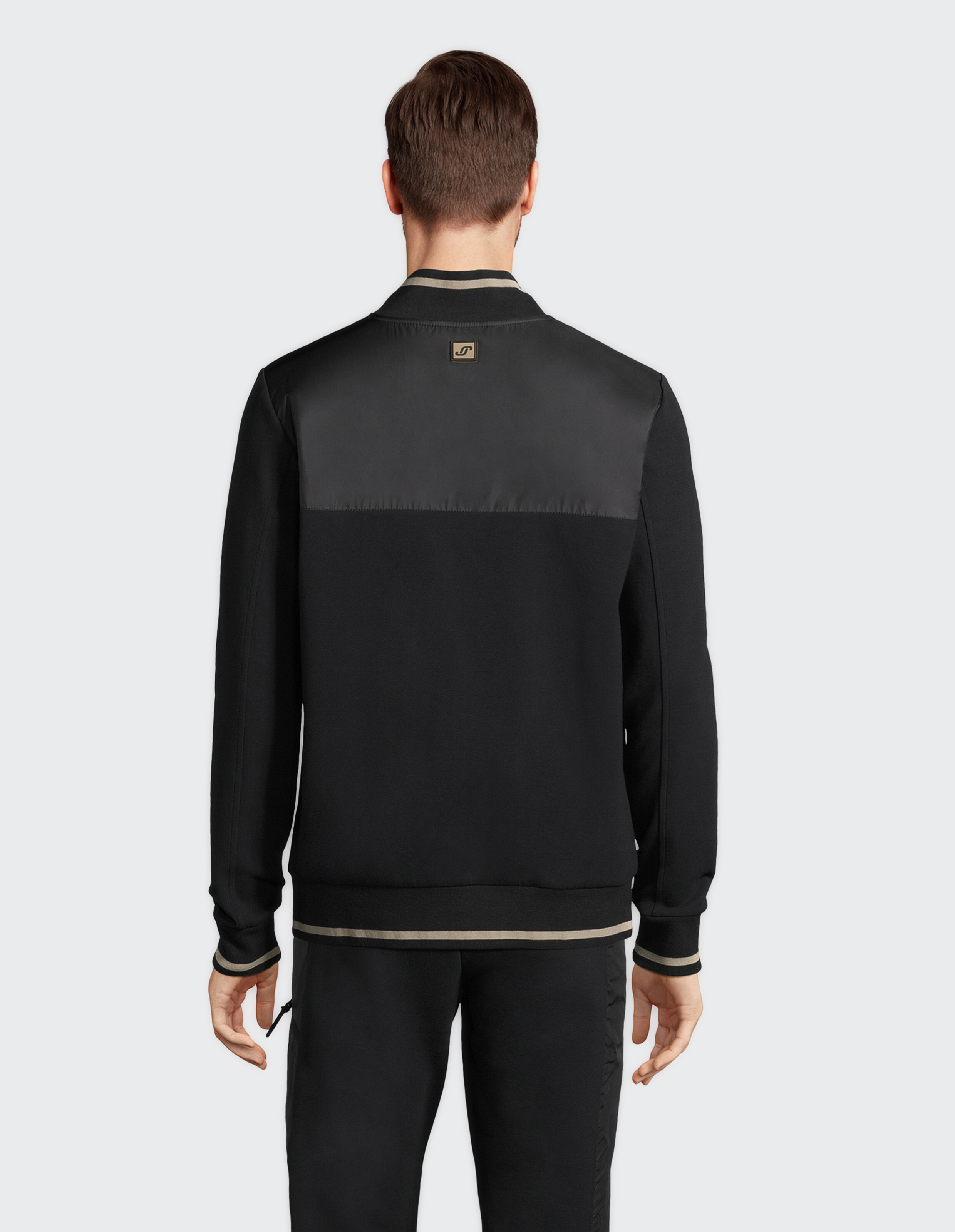 Rückansicht eines Mannes, der eine schwarze, lässige Bomberjacke mit beigen Besatzdetails trägt.