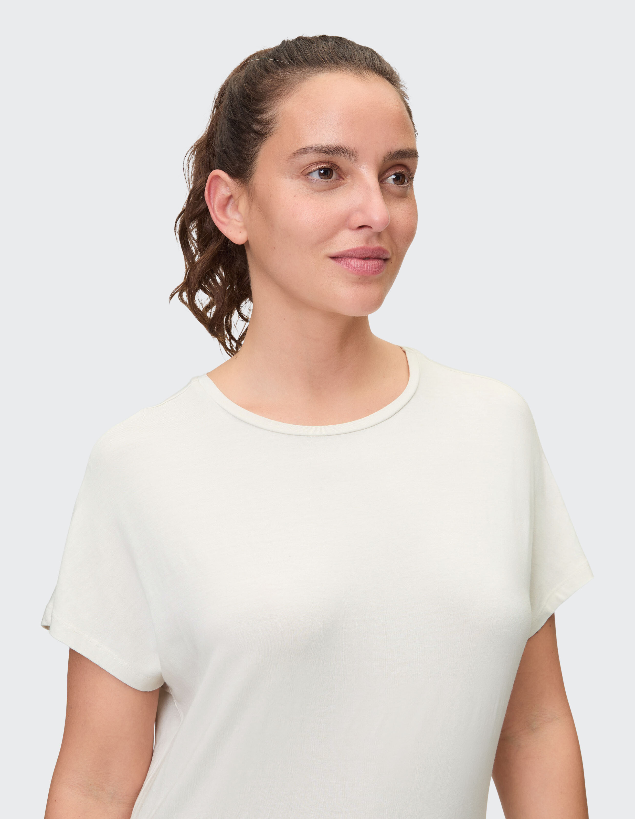 Nahaufnahme einer Frau, die ein hellcremefarbenes Freizeit-T-Shirt mit hochgekrempelten Ärmeln trägt.
