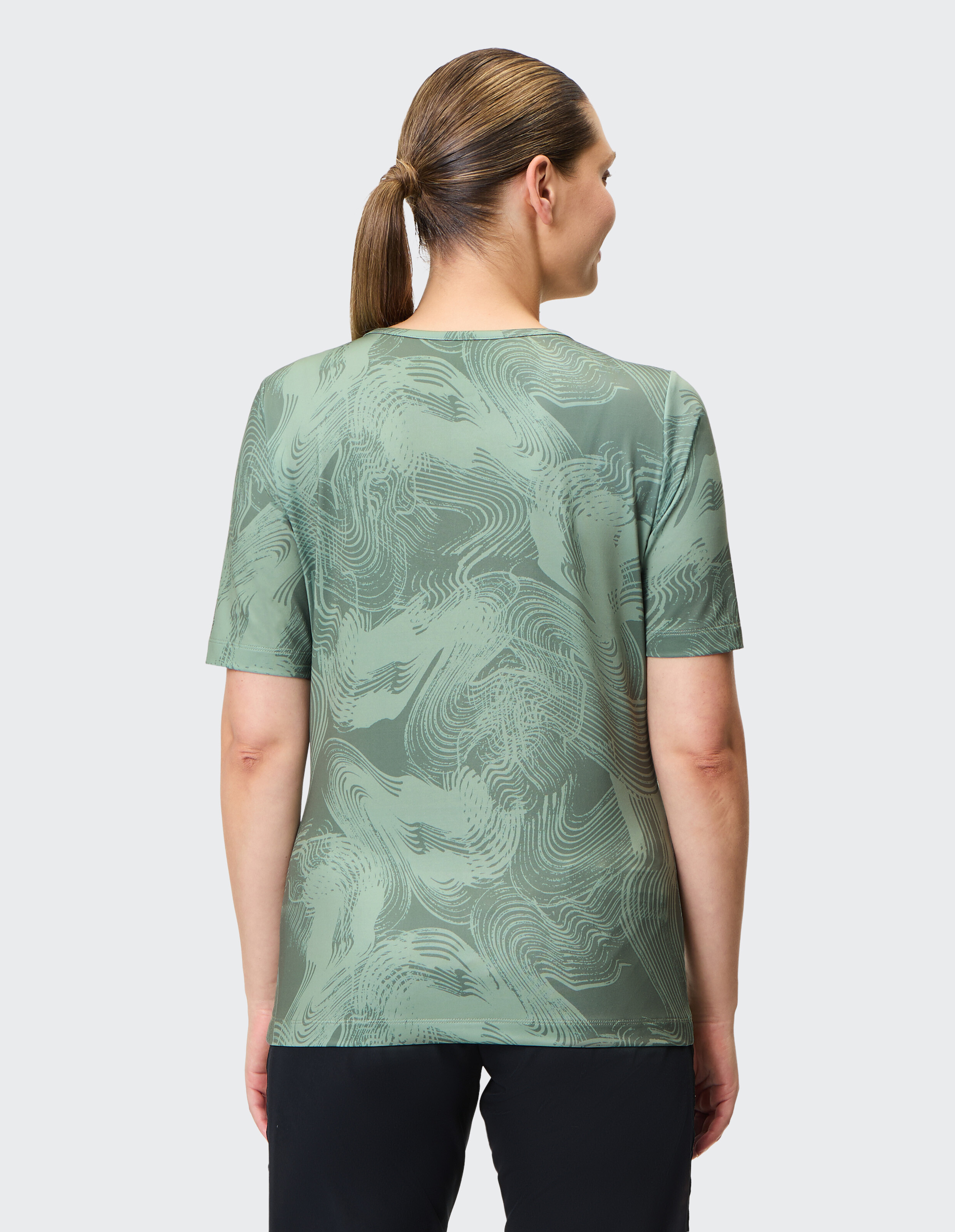 Frau trägt ein grün gemustertes Freizeit-T-Shirt, Rückansicht, Studioaufnahme.