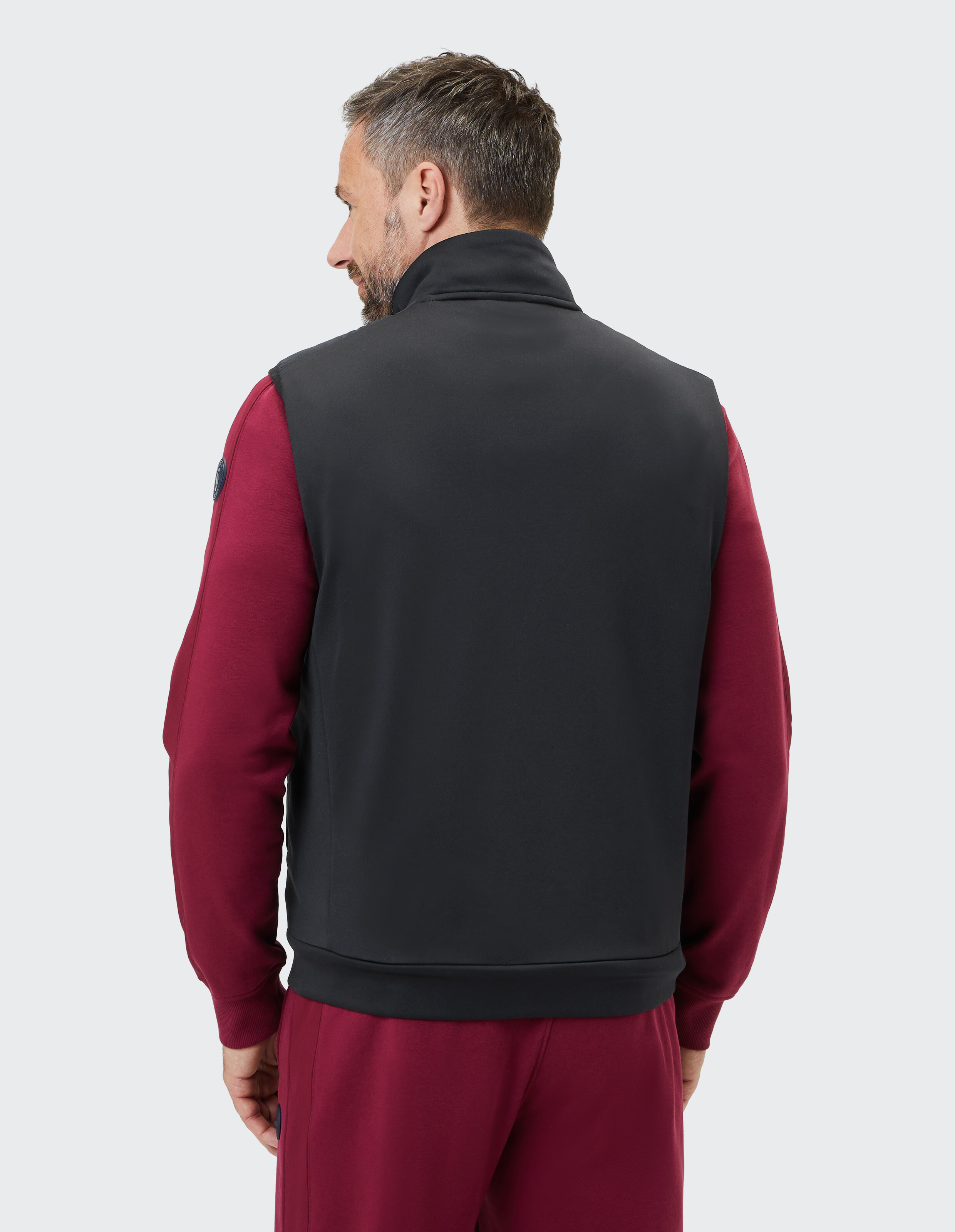 Mann trägt eine schwarze ärmellose Weste über einem kastanienbraunen Langarmhemd im lässigen Stil.