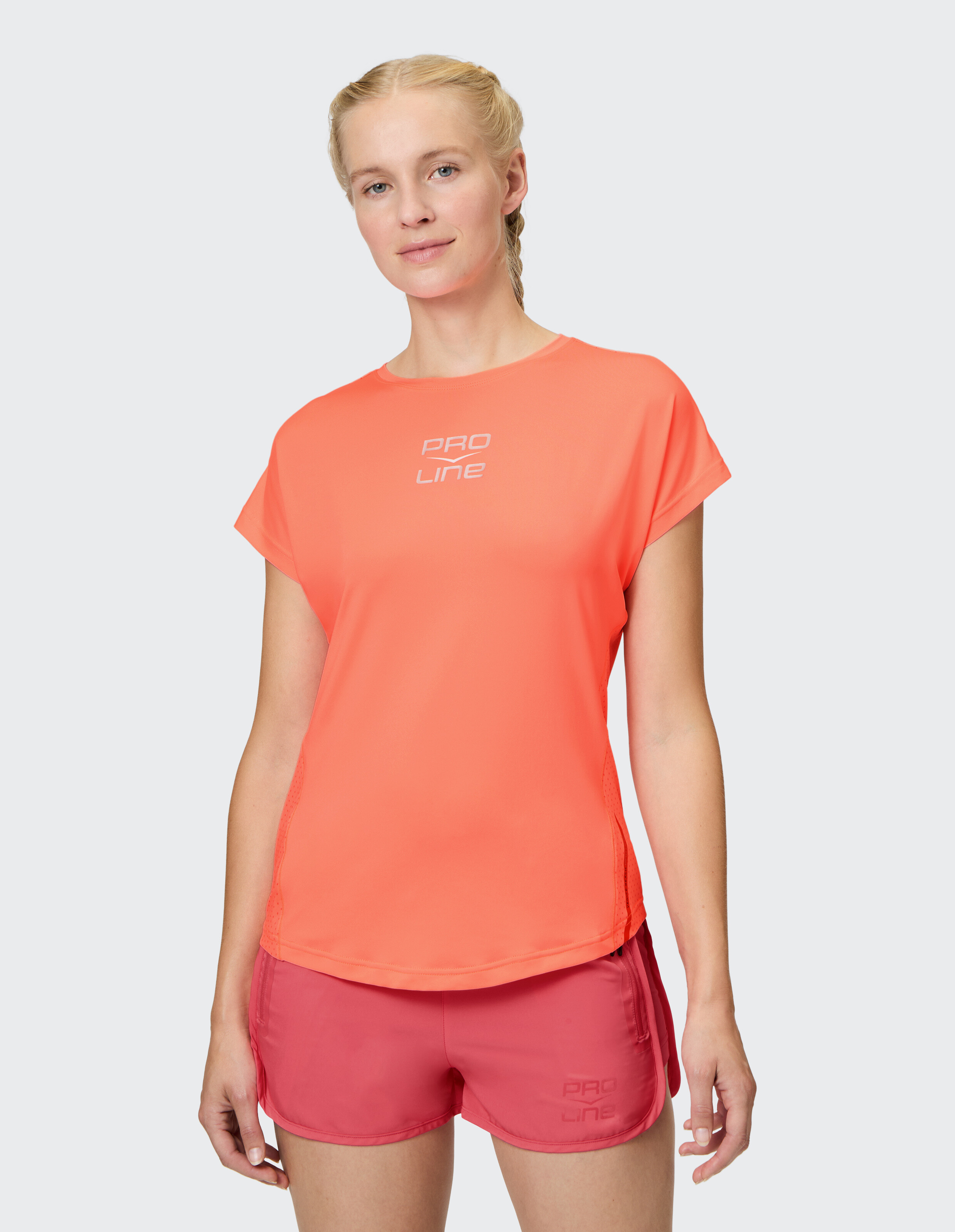 Frau trägt ein leuchtend orangefarbenes PRO LINE-T-Shirt und rosa Shorts, ideal für Freizeitkleidung.