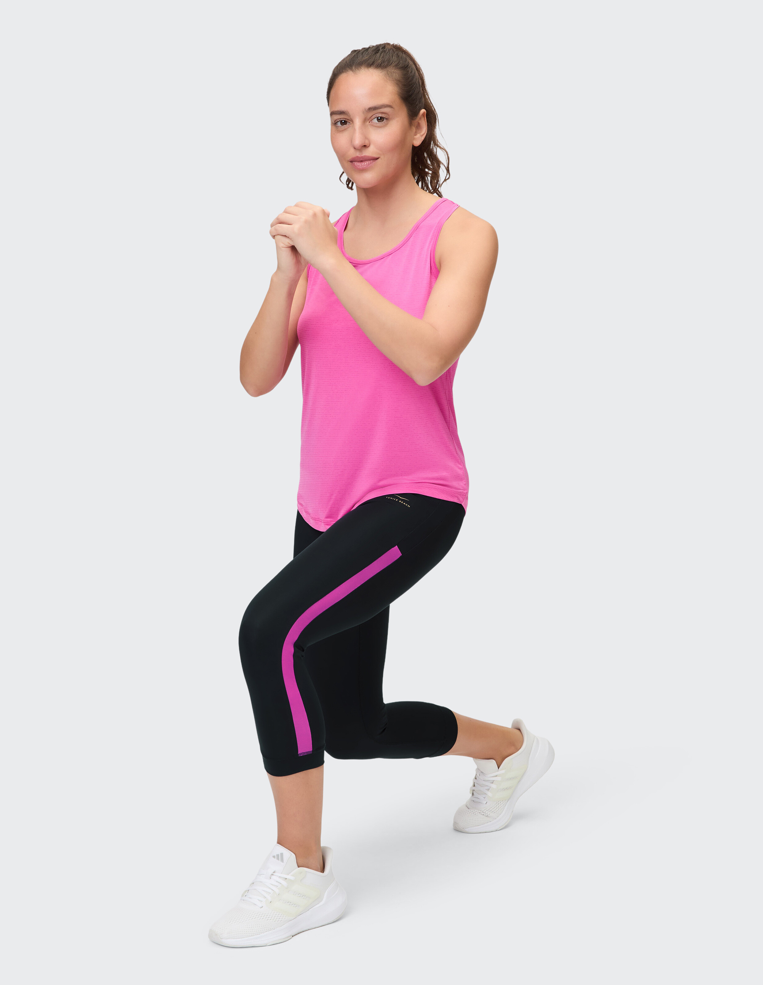 Frau in einem rosa Tanktop und schwarzen, kurzen Leggings für lässige Aktivkleidung.