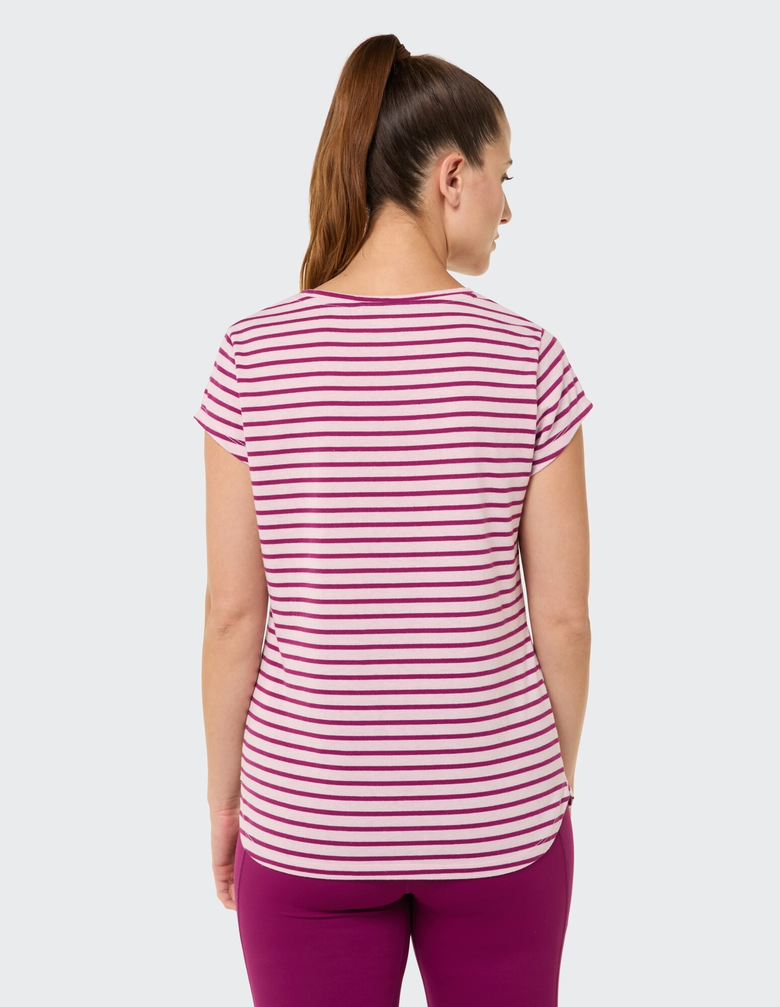 Rückansicht einer Frau in einem rosa gestreiften Freizeit-T-Shirt und einer lila Hose.