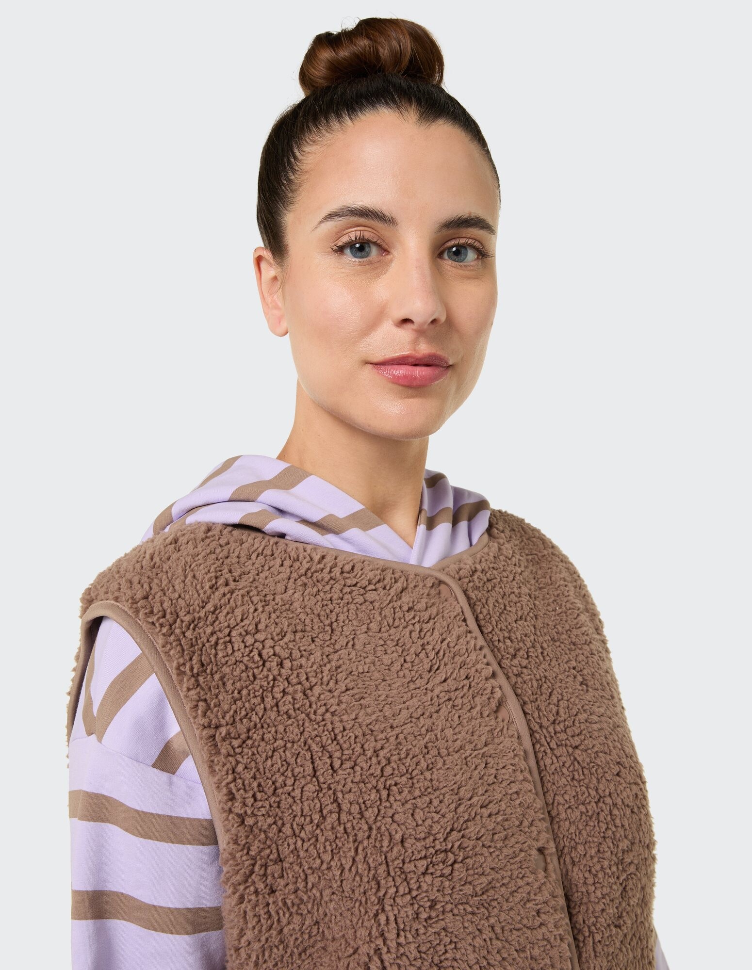 Kuschelige braune Fleeceweste über einem gestreiften lavendelfarbenen Kapuzenpullover, perfekt für Freizeitkleidung.