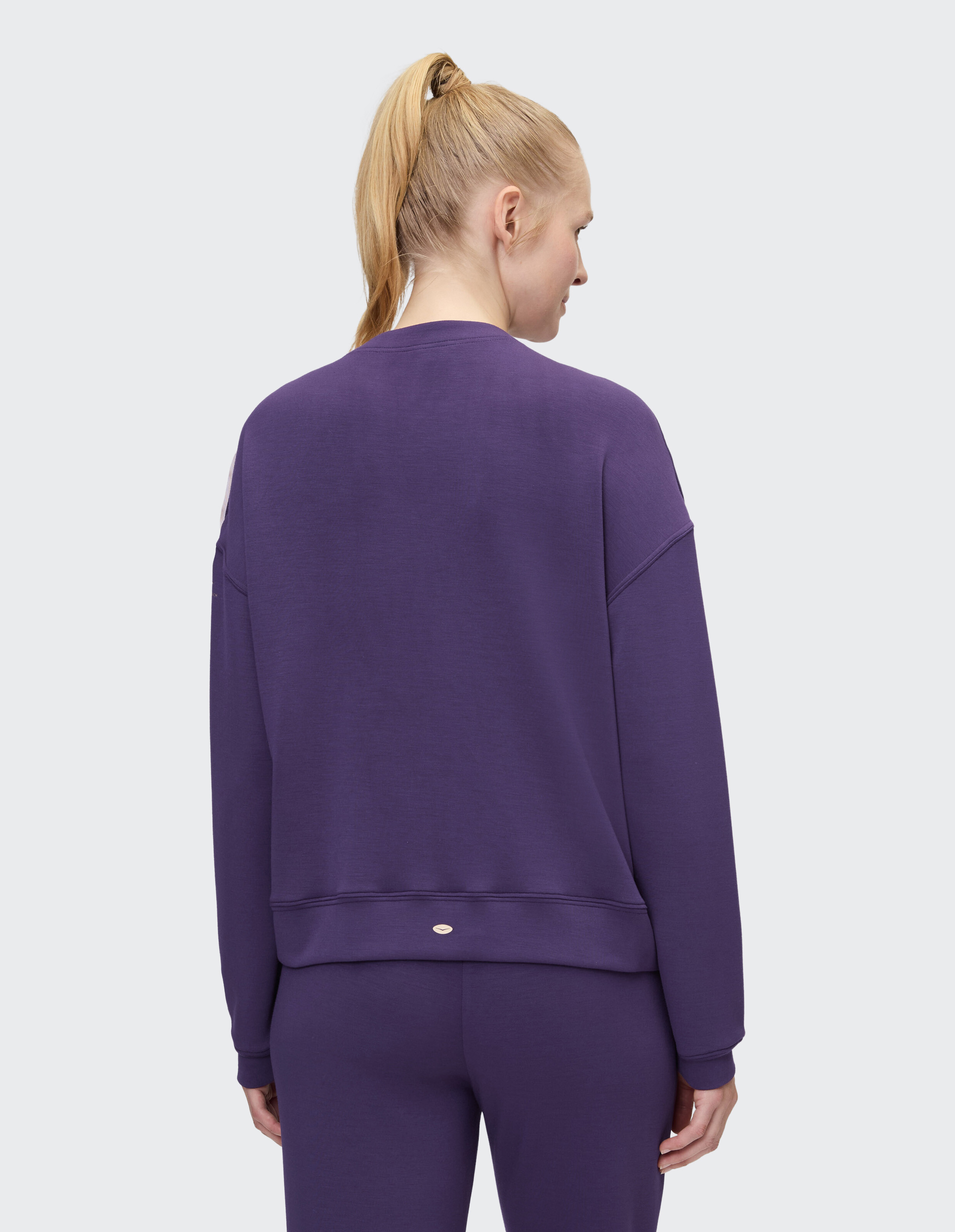 Frau trägt ein gemütliches lilafarbenes Freizeit-Sweatshirt zum Faulenzen, Rückansicht.