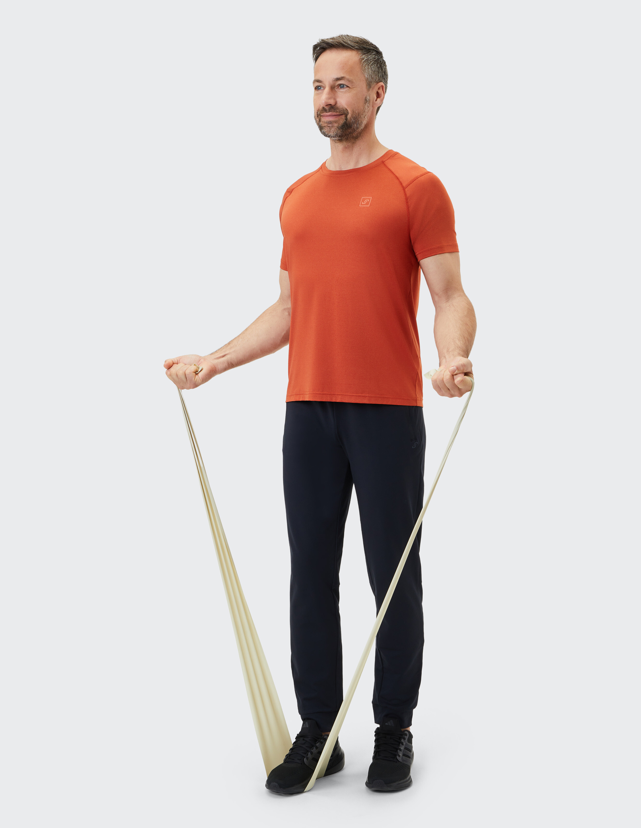 Mann in orangefarbenem T-Shirt und dunkler Jogginghose trainiert mit einem Widerstandsband.