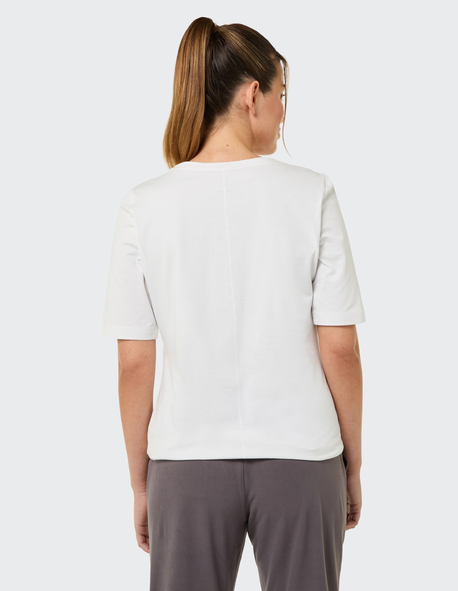 Rückansicht einer Frau in einem weißen Freizeit-T-Shirt und einer grauen Hose.
