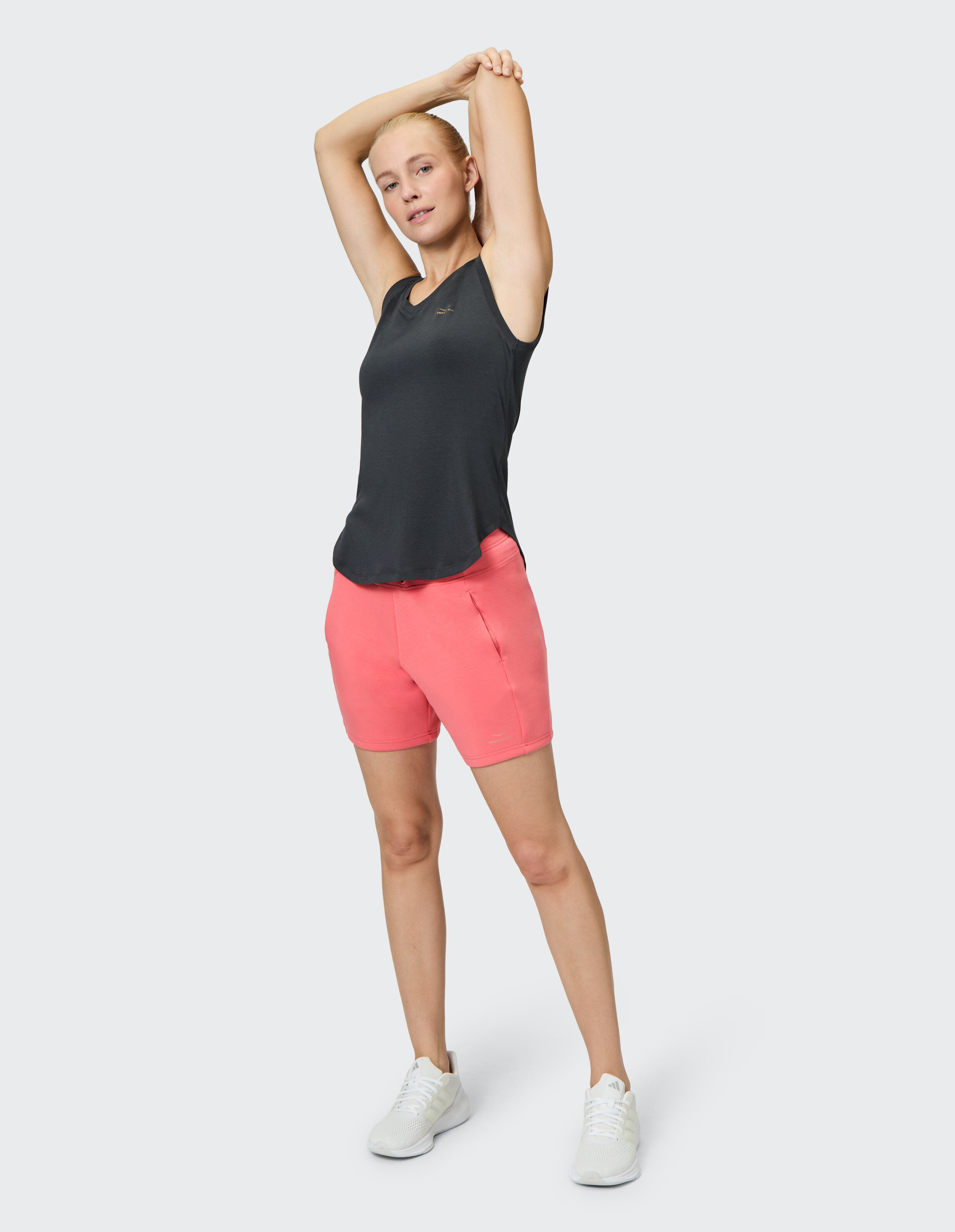 Frau dehnt sich in einem schwarzen Tanktop und rosa Shorts, perfekt für Freizeitkleidung.