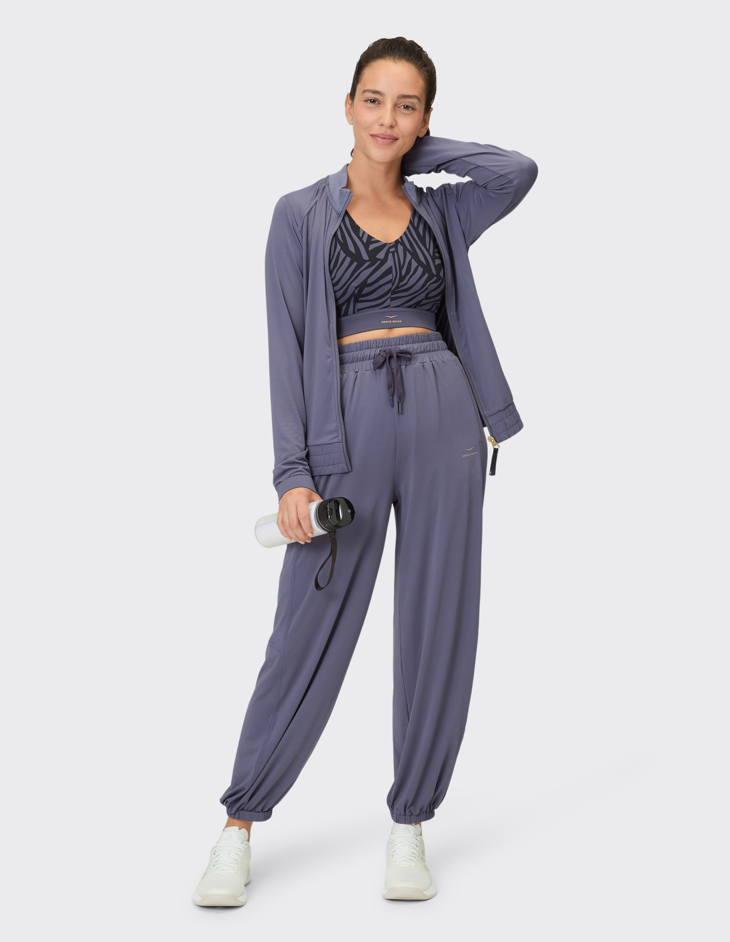 Frau trägt ein lilafarbenes Lounge-Set mit gemustertem Sport-BH und Jogginghose.