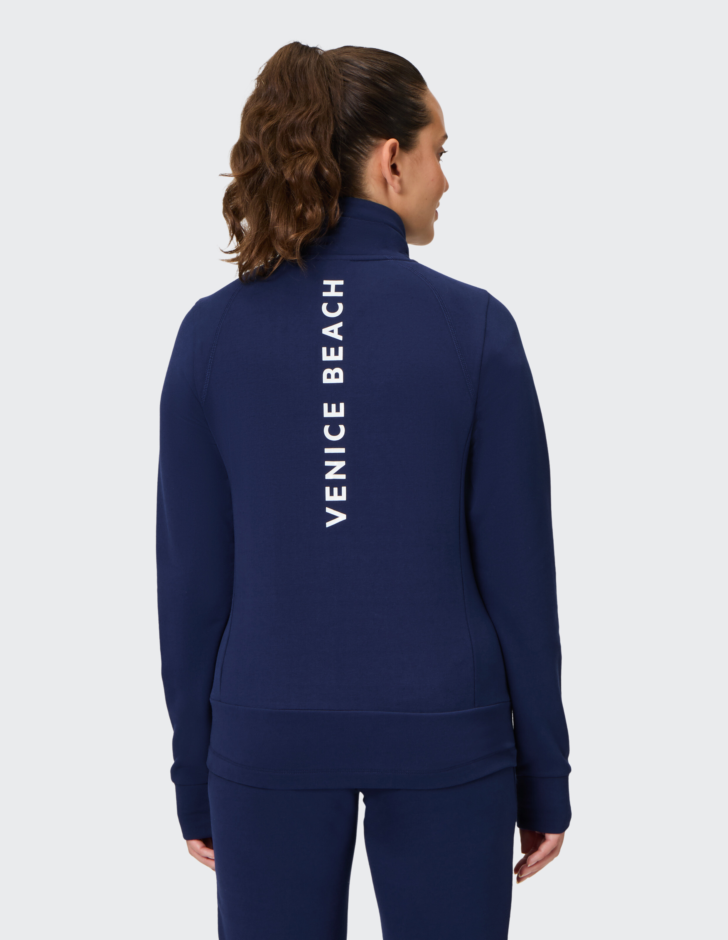 Frau trägt eine marineblaue Jacke mit Reißverschluss und dem Text „Venice Beach“ auf der Rückseite.