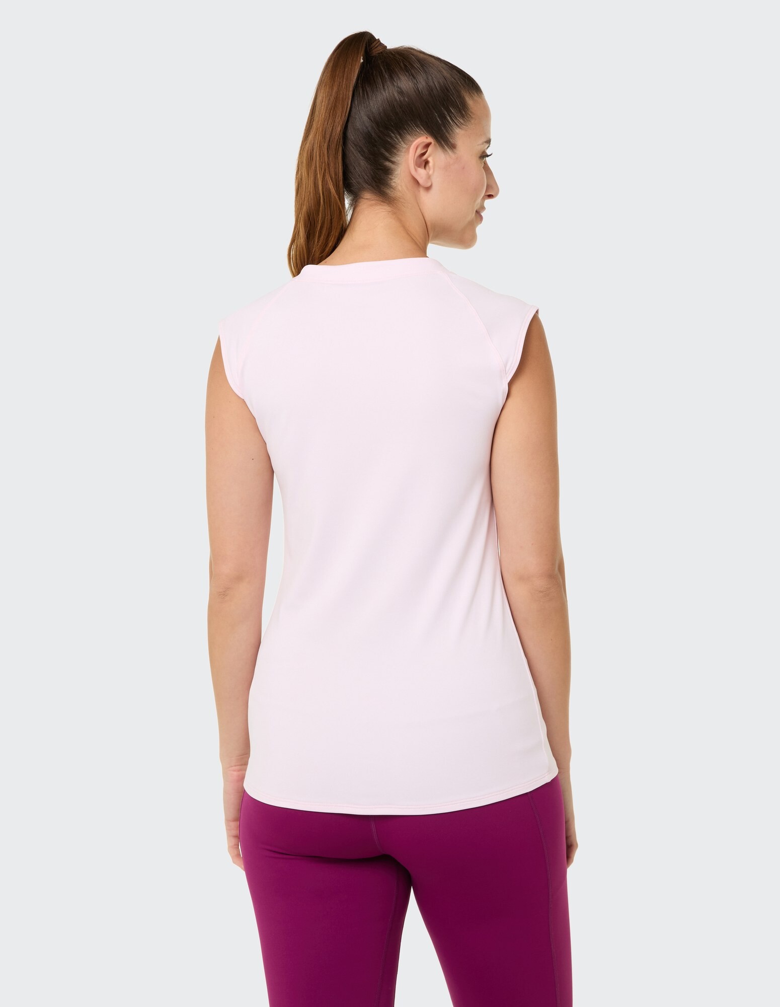 Rückansicht einer Frau in einem rosa ärmellosen Top und lila Leggings.