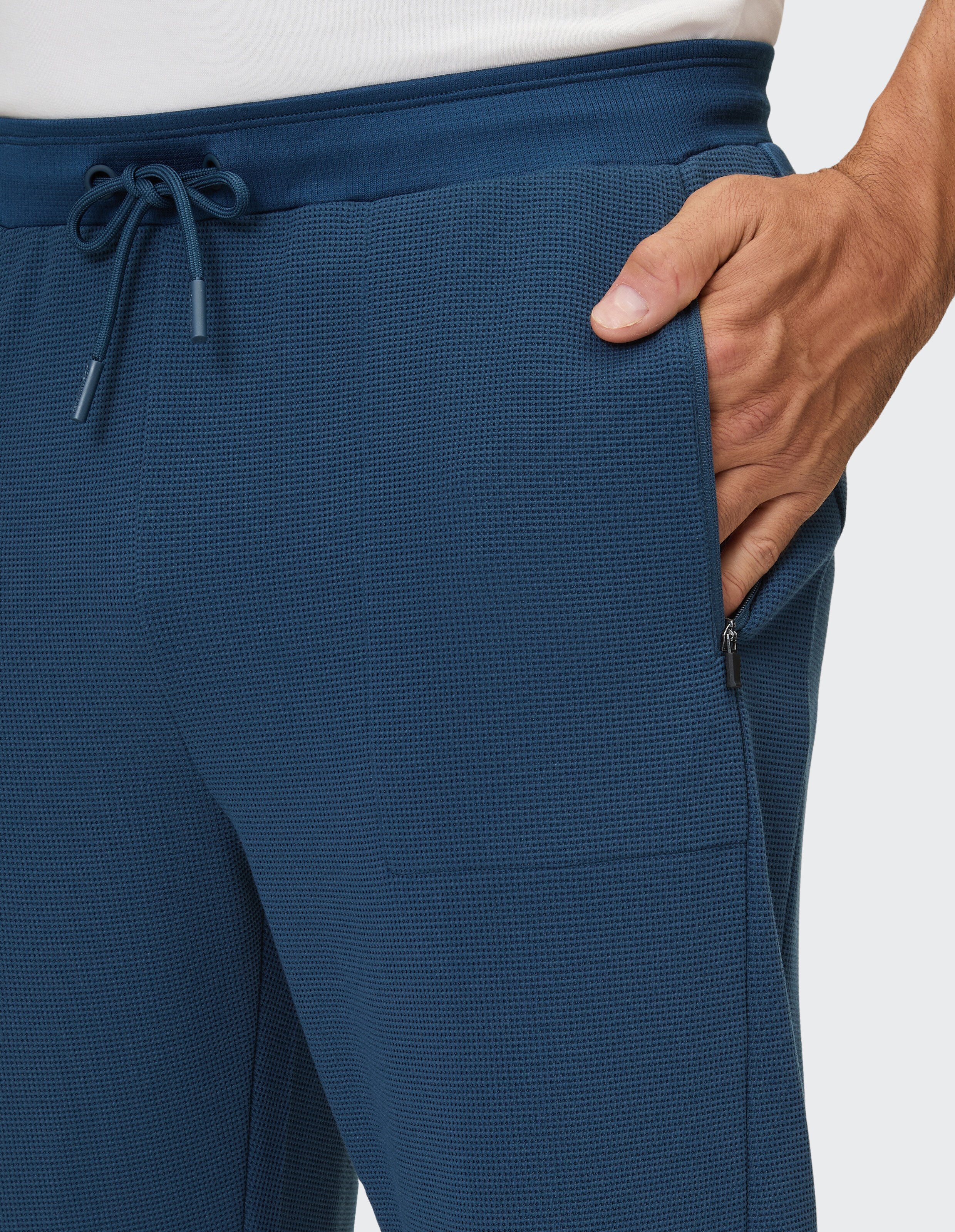Nahaufnahme einer blauen strukturierten Herren-Jogginghose mit Kordelzug und Reißverschlusstasche.