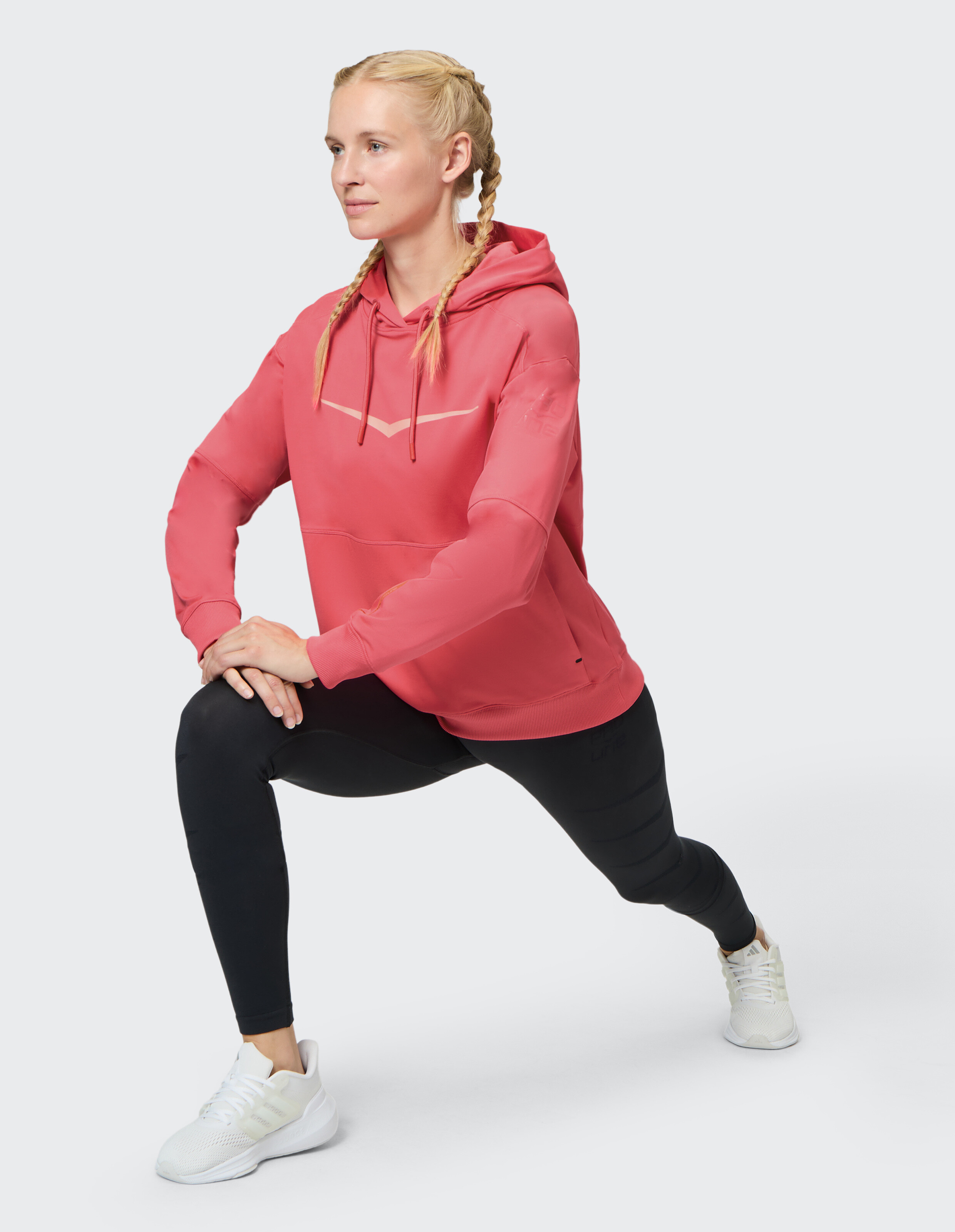 Frau in einem roten Kapuzenpullover und schwarzen Leggings macht einen Ausfallschritt, perfekt für lässige Aktivkleidung.