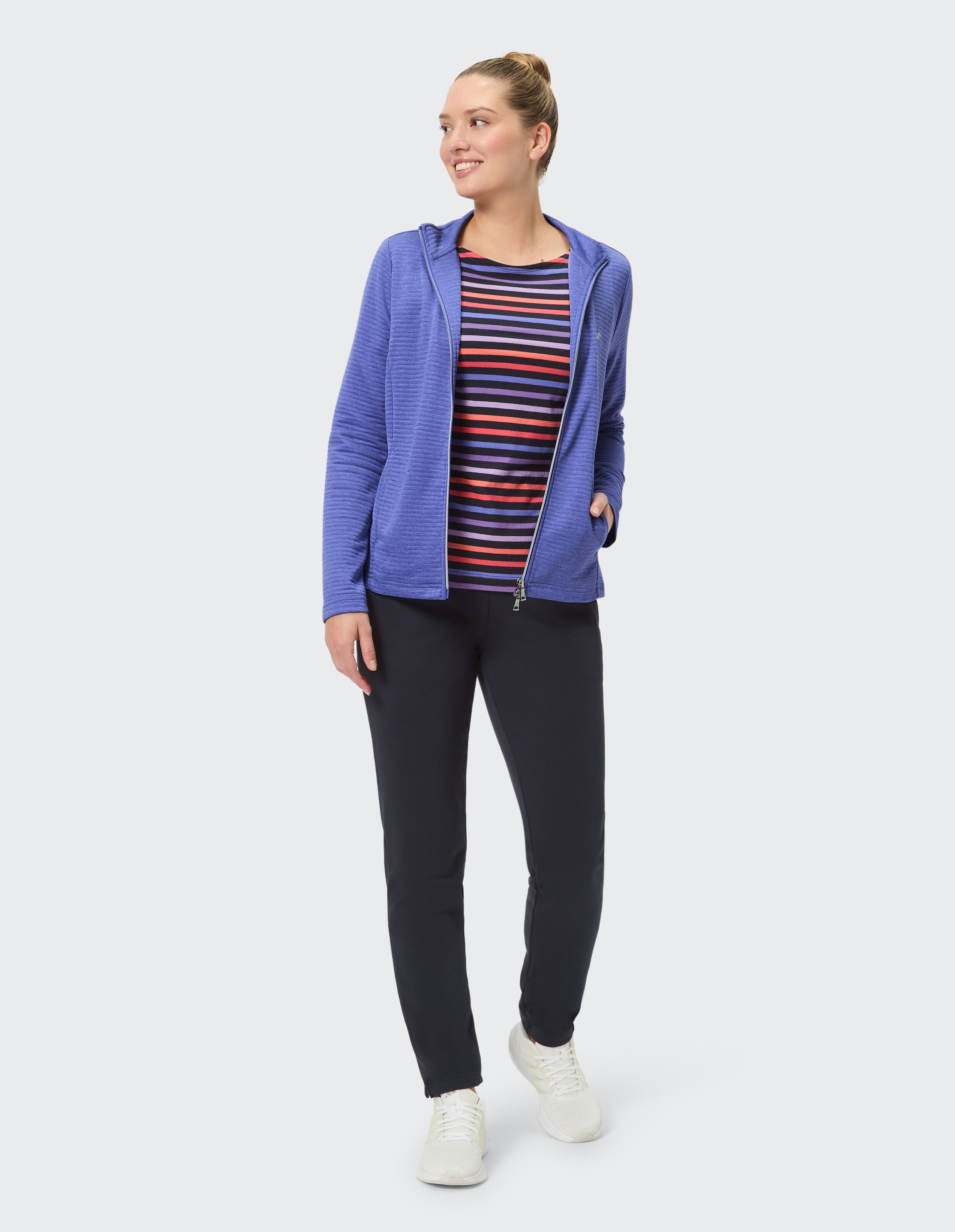 Frau in einem gemütlichen blauen Kapuzenpullover mit Reißverschluss und gestreiftem Oberteil, gepaart mit einer schwarzen Hose.