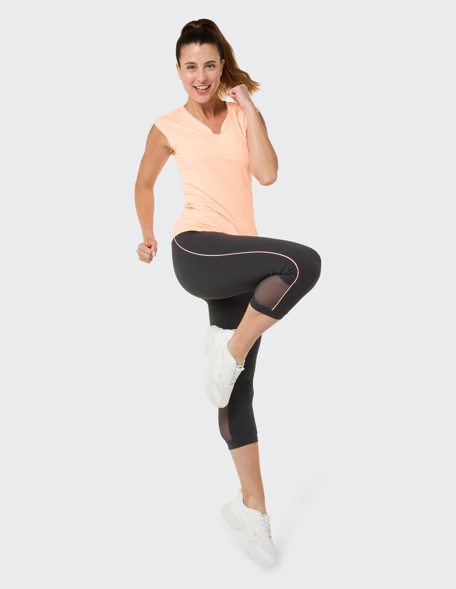 Frau in pfirsichfarbenem Top mit V-Ausschnitt und schwarzen Leggings mit Netzstoff, perfekt für lässige Workouts.
