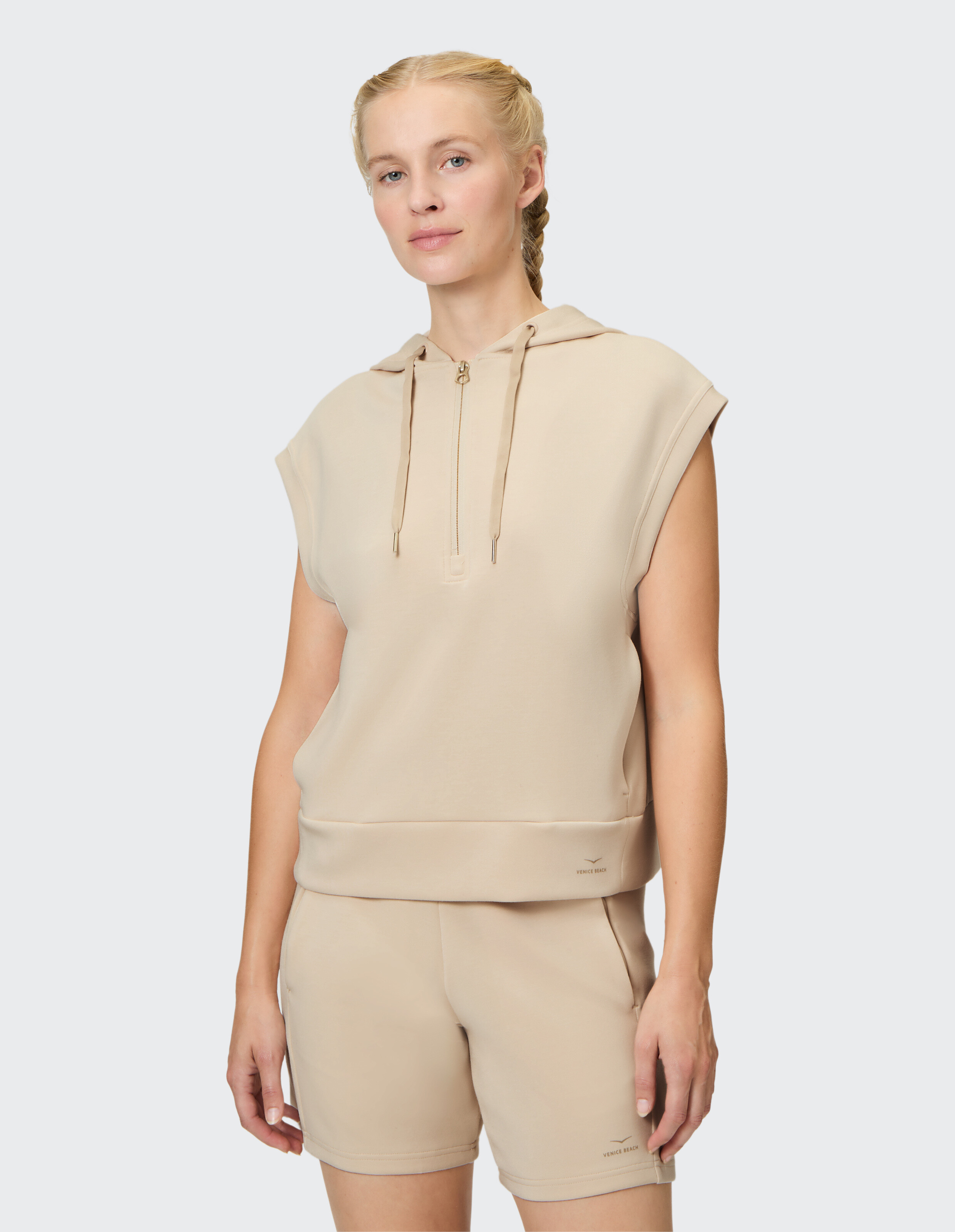 Frau trägt einen beigen ärmellosen Kapuzenpullover und passende Shorts für lässige Loungewear.