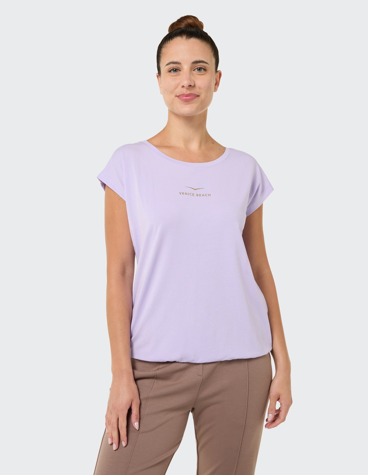 Frau trägt ein fliederfarbenes, lässiges T-Shirt mit „VENICE BEACH“-Aufdruck, gestylt für Komfort.