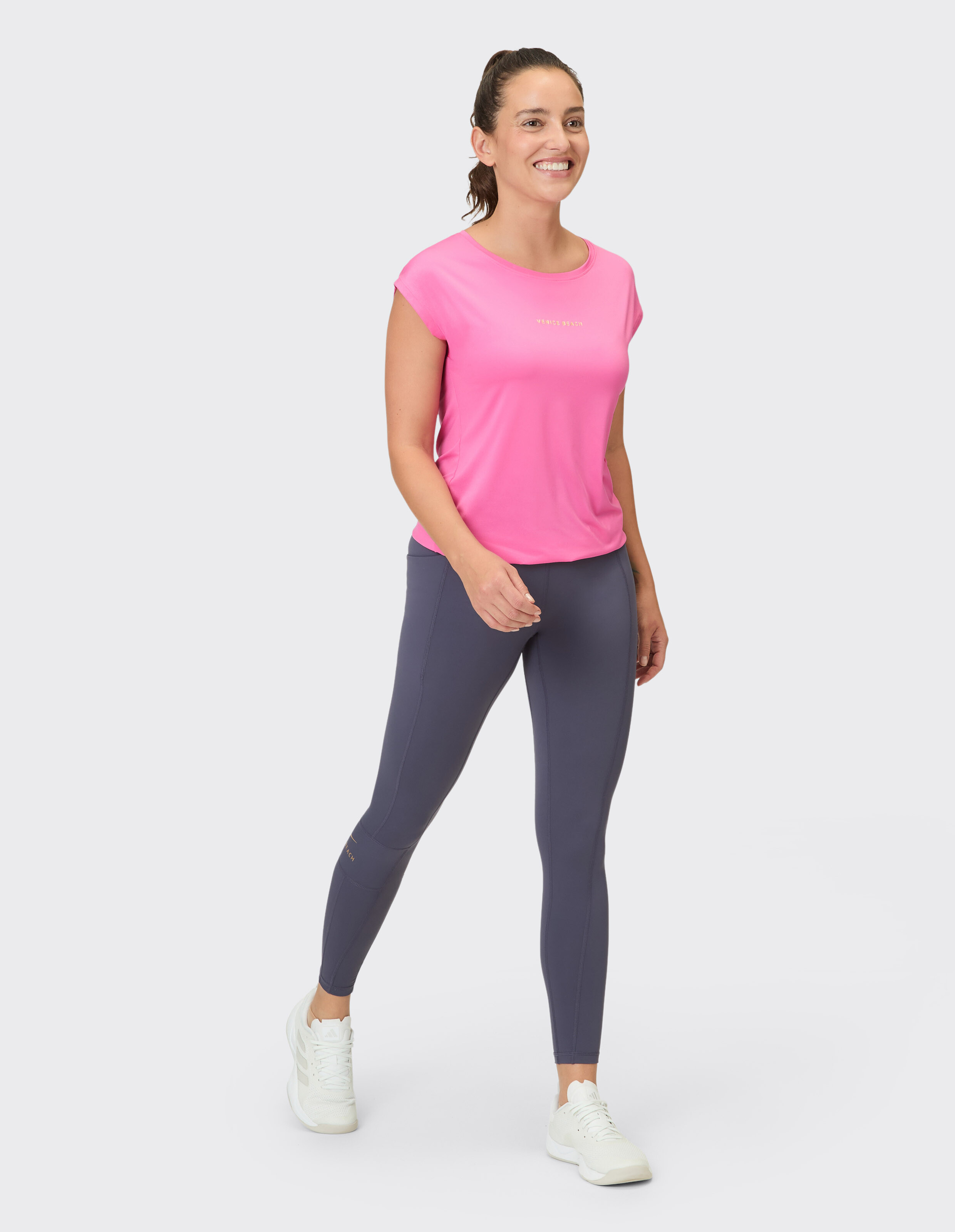 Lächelnde Frau in rosa Top und grauen Leggings, perfekt für Freizeitkleidung.