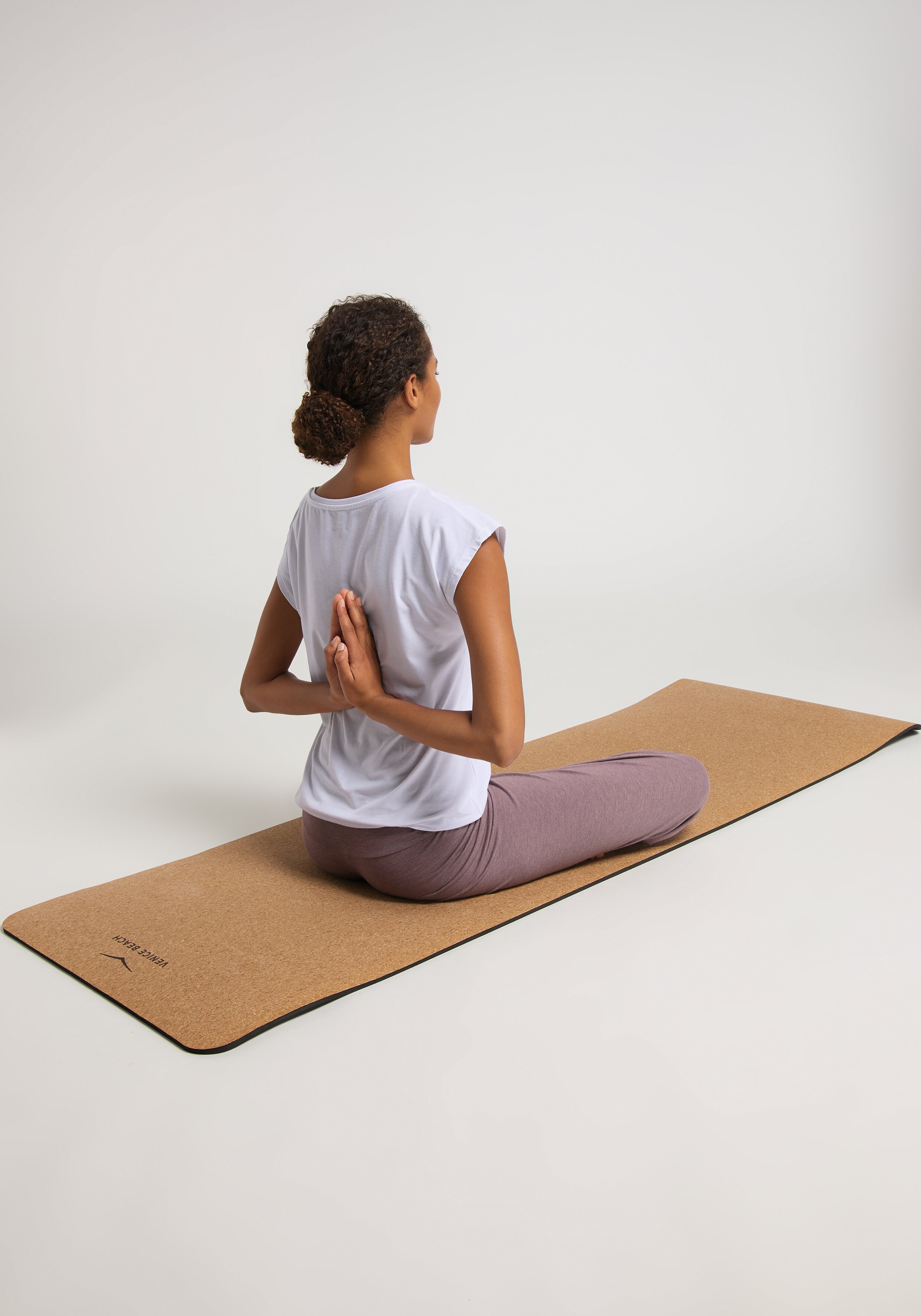 Frau in weißem T-Shirt und lila Leggings macht Yoga auf einer Korkmatte.
