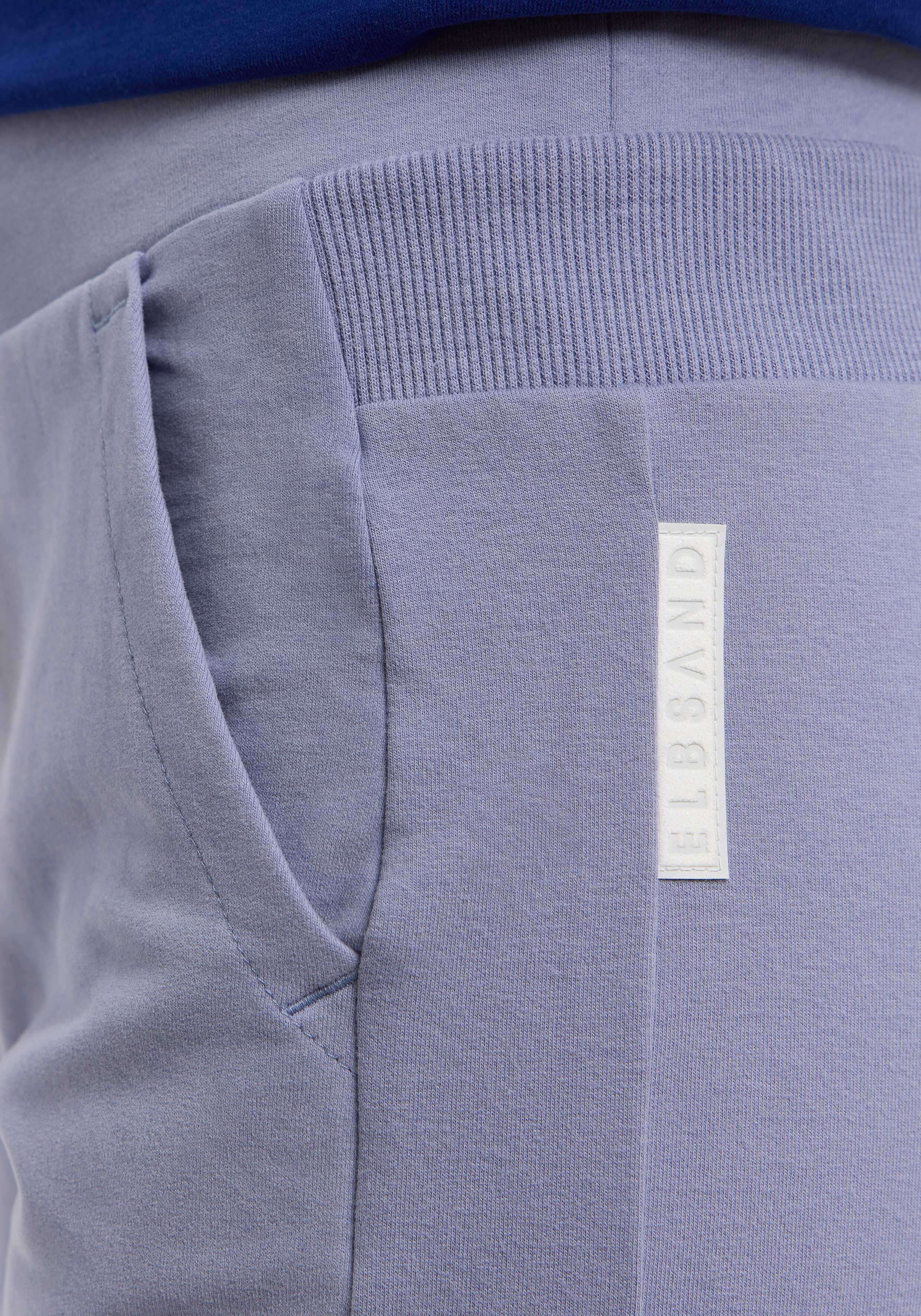 Nahaufnahme der blauen ELBSAND-Loungehose mit geripptem Bund und Logo-Patch.