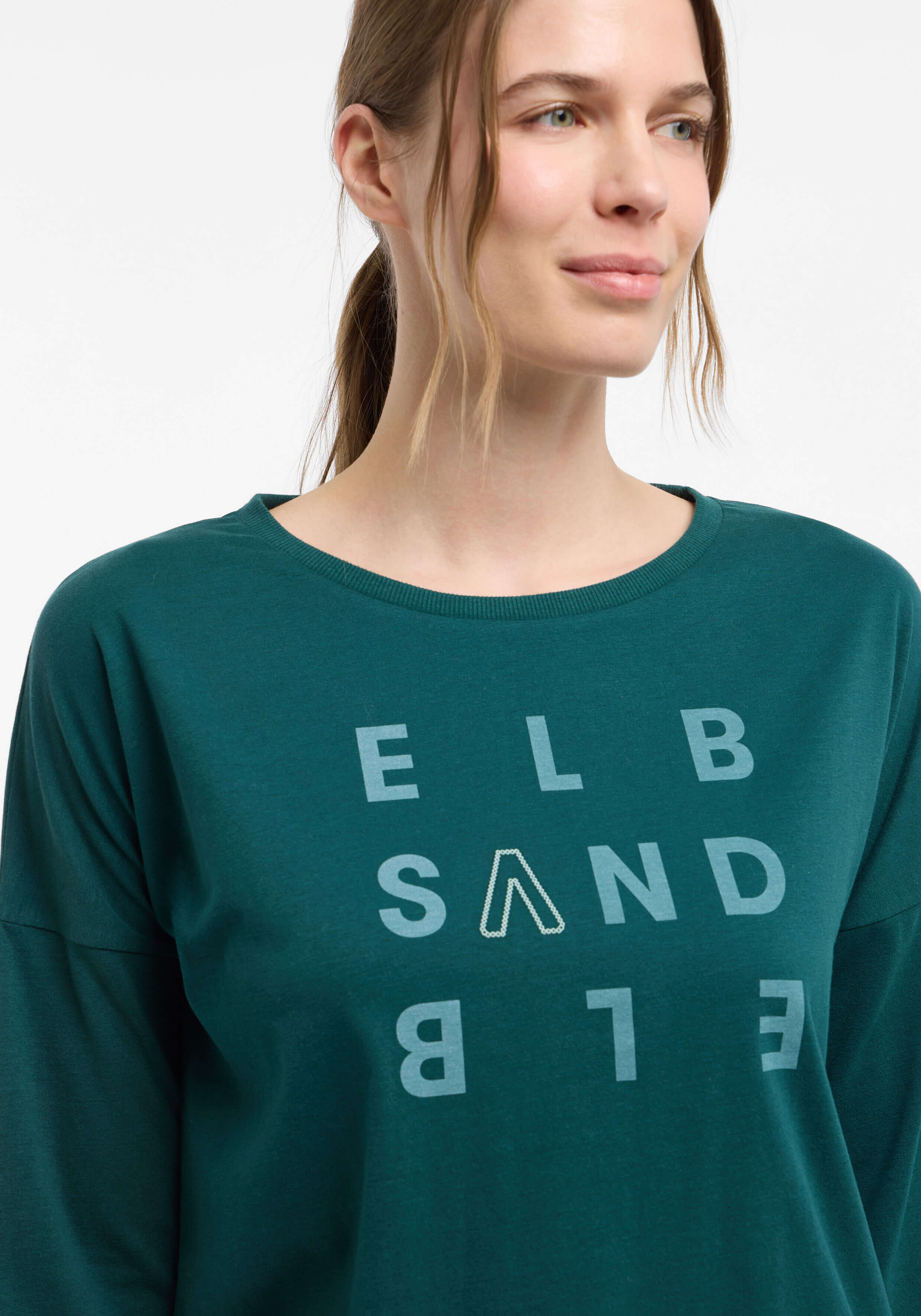 Frau trägt ein dunkelgrünes ELBSAND Langarm-Freizeitshirt mit Logo-Print.