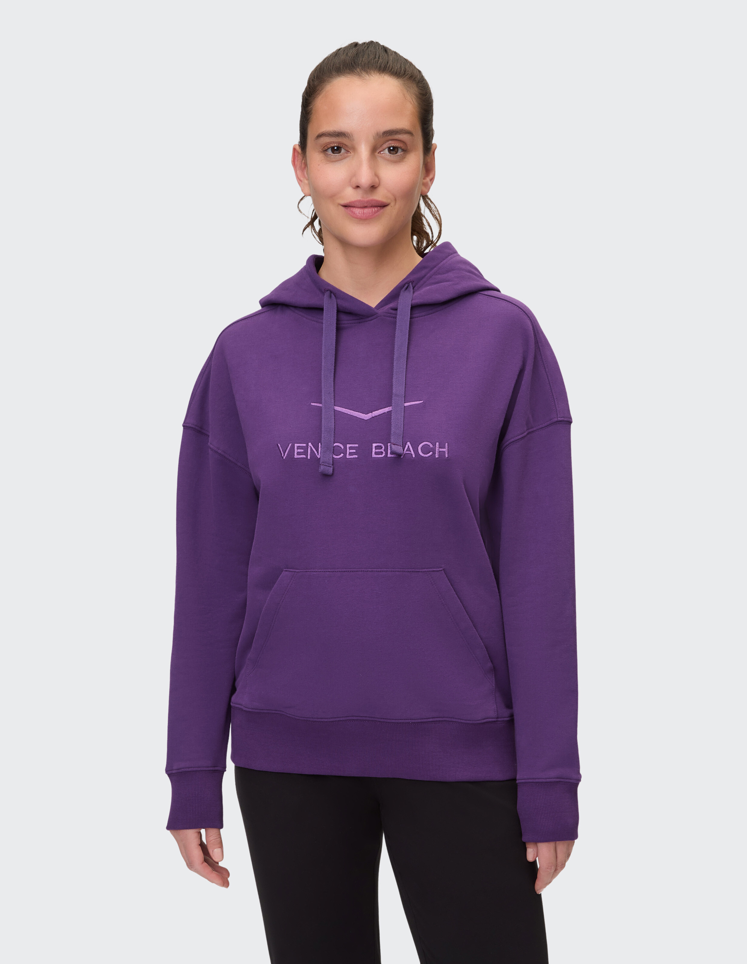 Frau trägt einen gemütlichen lilafarbenen Venice Beach-Hoodie mit Vordertasche und Kapuze mit Kordelzug.