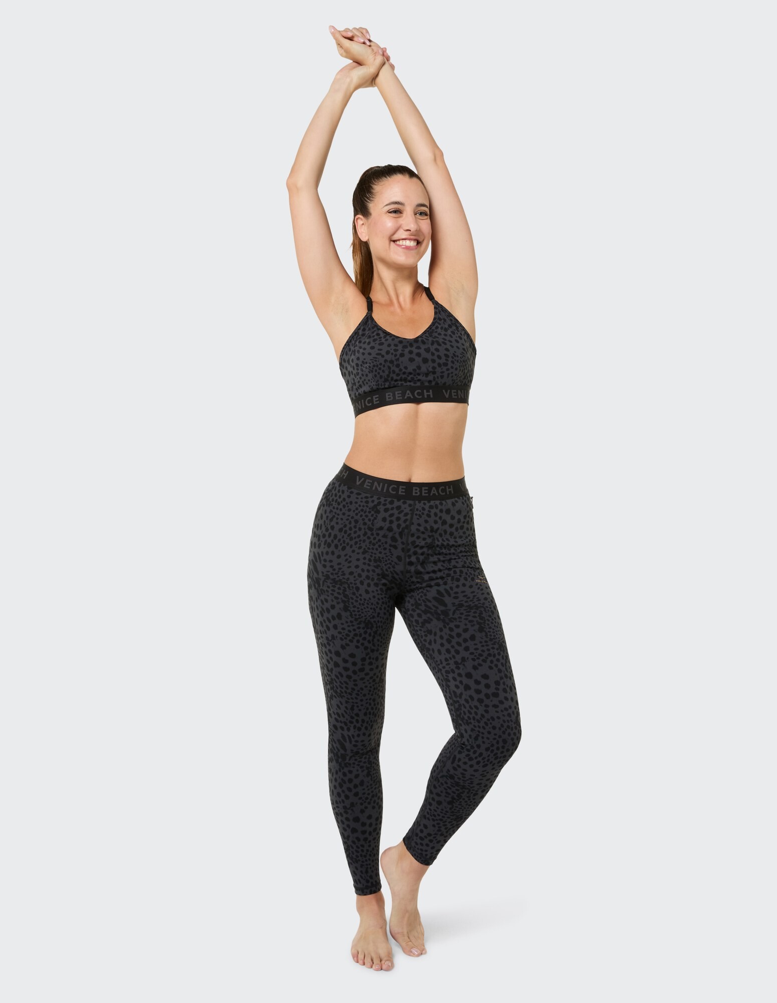 Lächelnde Frau in schwarzem Sport-BH und Leggings mit Leopardenmuster, die lässige Aktivkleidung präsentiert.