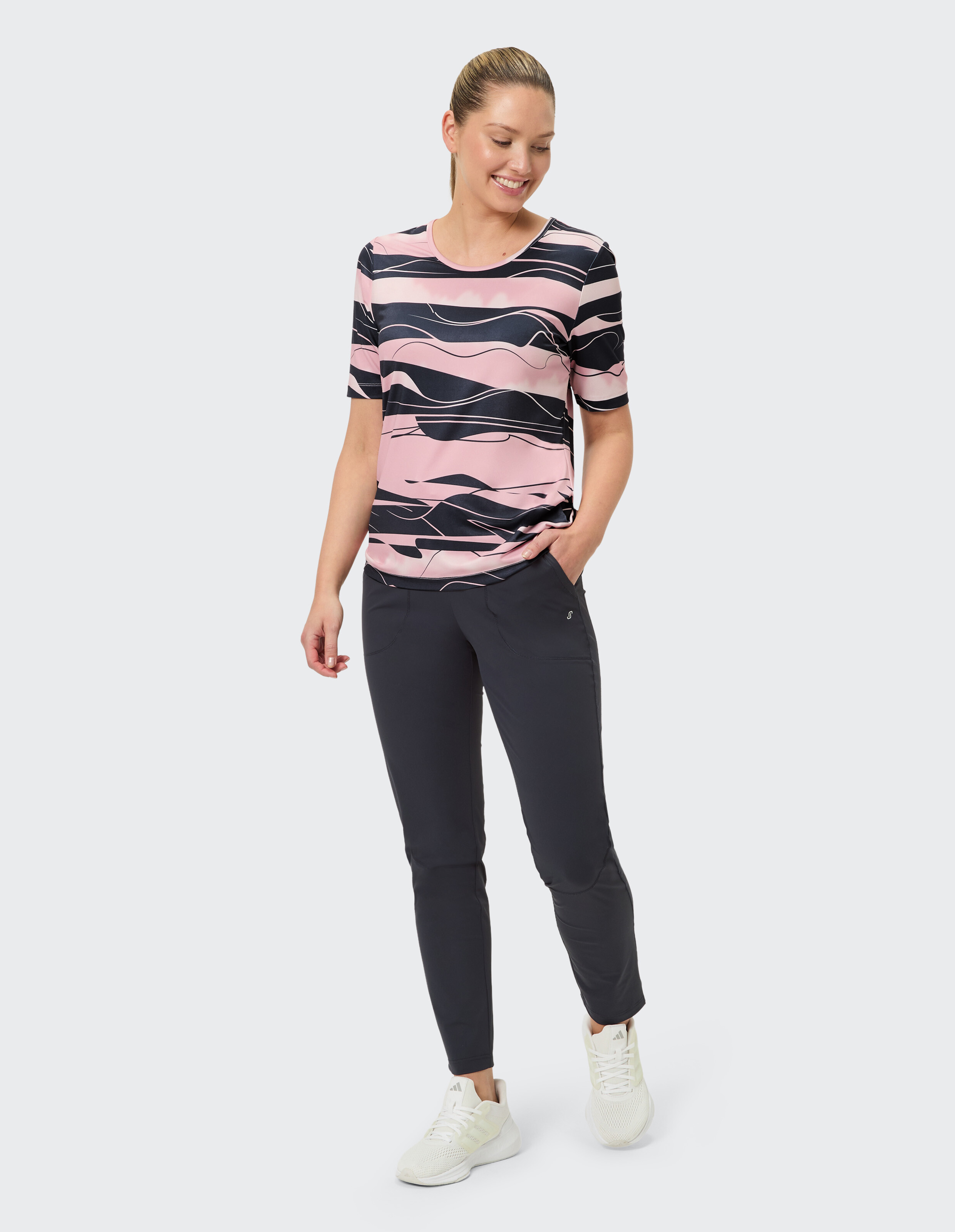 Frau in rosa und marineblau gestreiftem T-Shirt und dunkler Hose, lächelnd lässig.