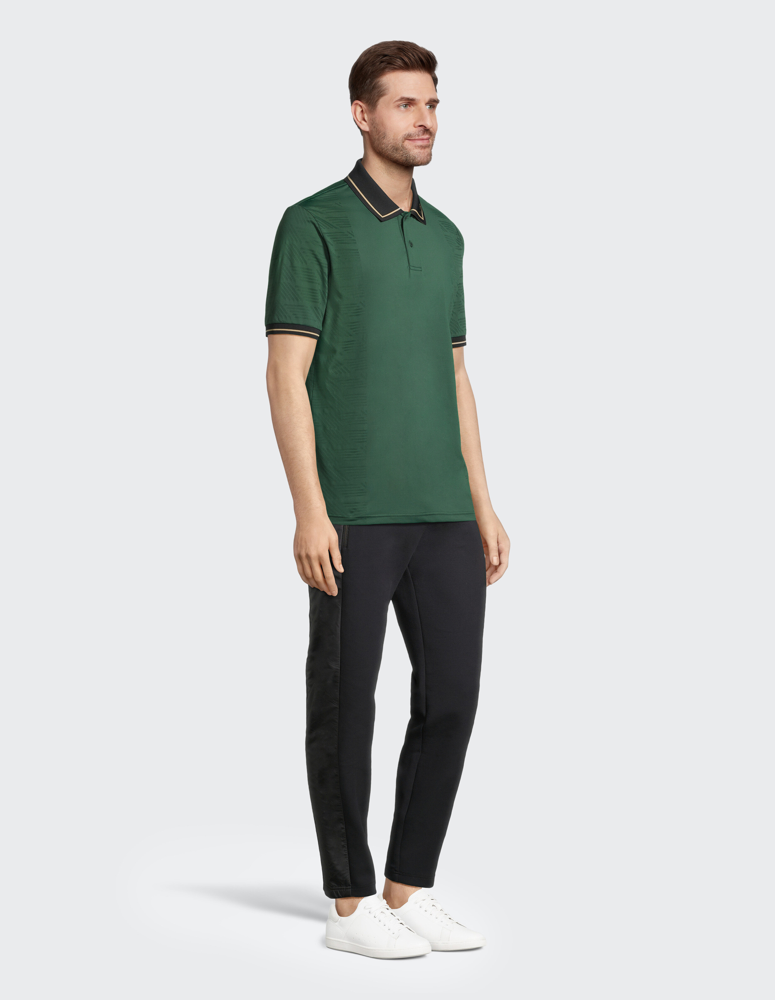 Mann trägt ein grünes Poloshirt mit schwarzem Besatz und eine schwarze Hose, lässig gestylt.