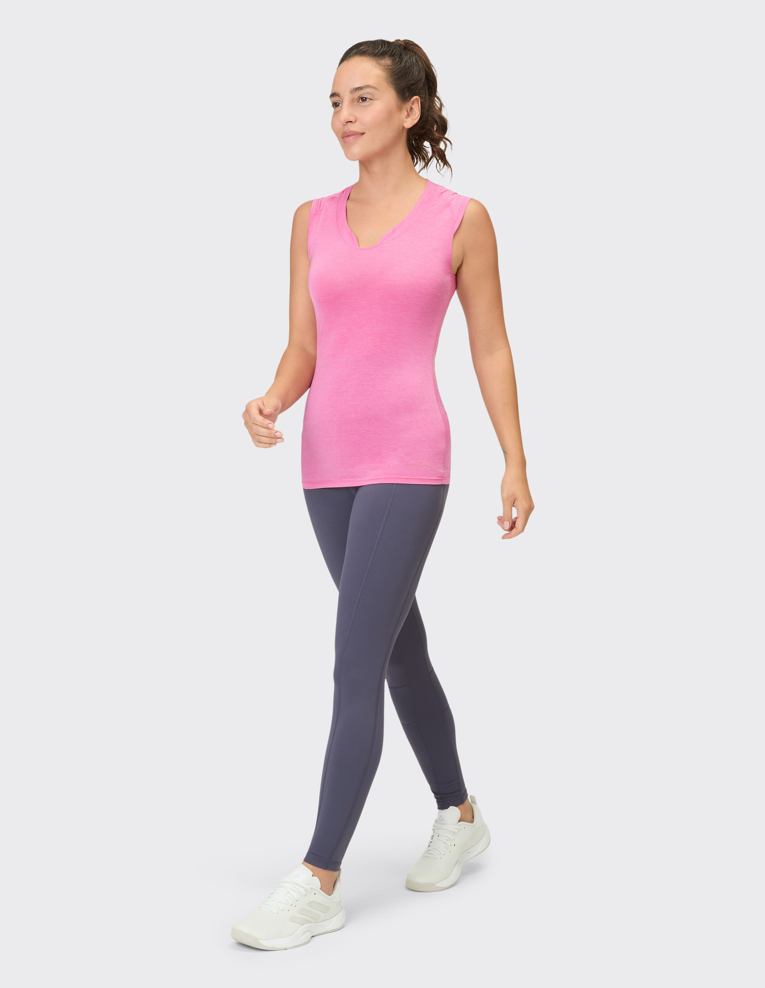 Frau trägt ein rosa ärmelloses Top und graue Leggings für einen lässigen, sportlichen Look.
