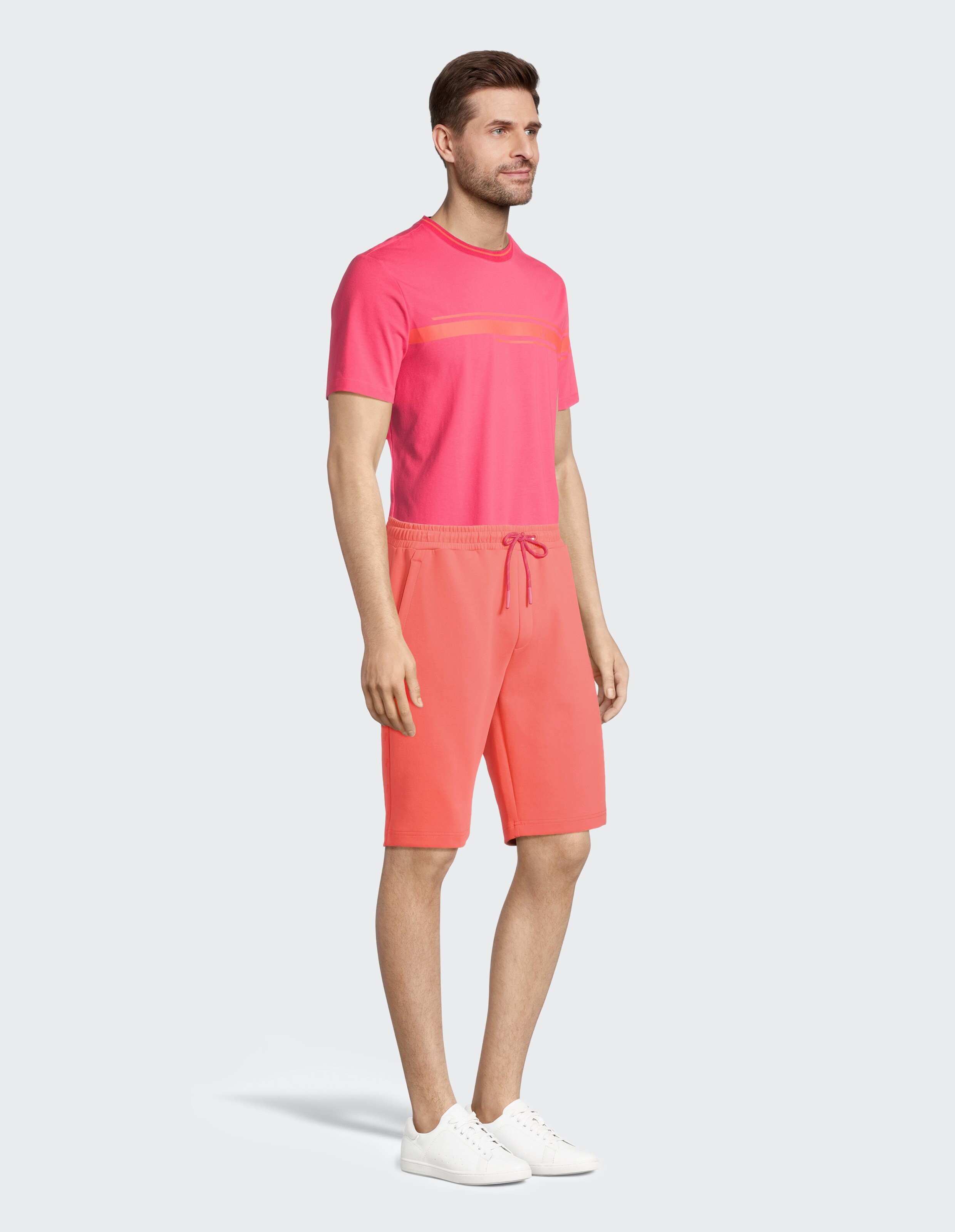 Mann trägt ein rosa T-Shirt und korallenrote Freizeitshorts für einen bequemen, stilvollen Look.