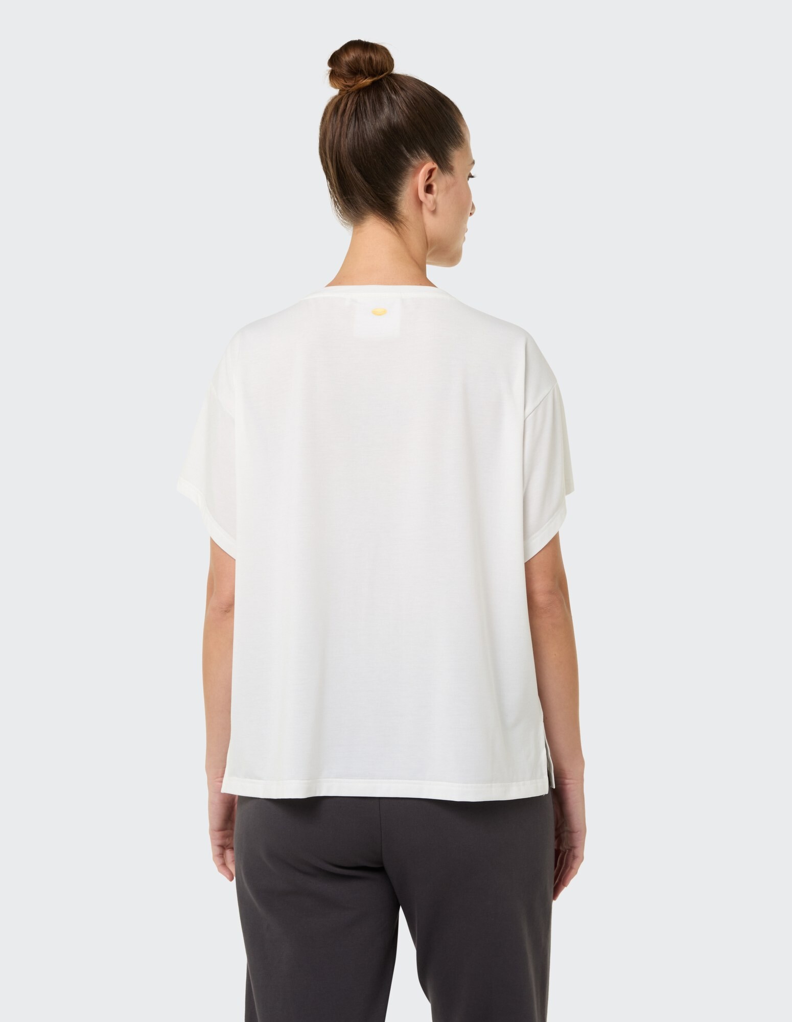 Rückansicht einer Frau, die ein weißes Freizeit-T-Shirt und eine dunkle Hose trägt.