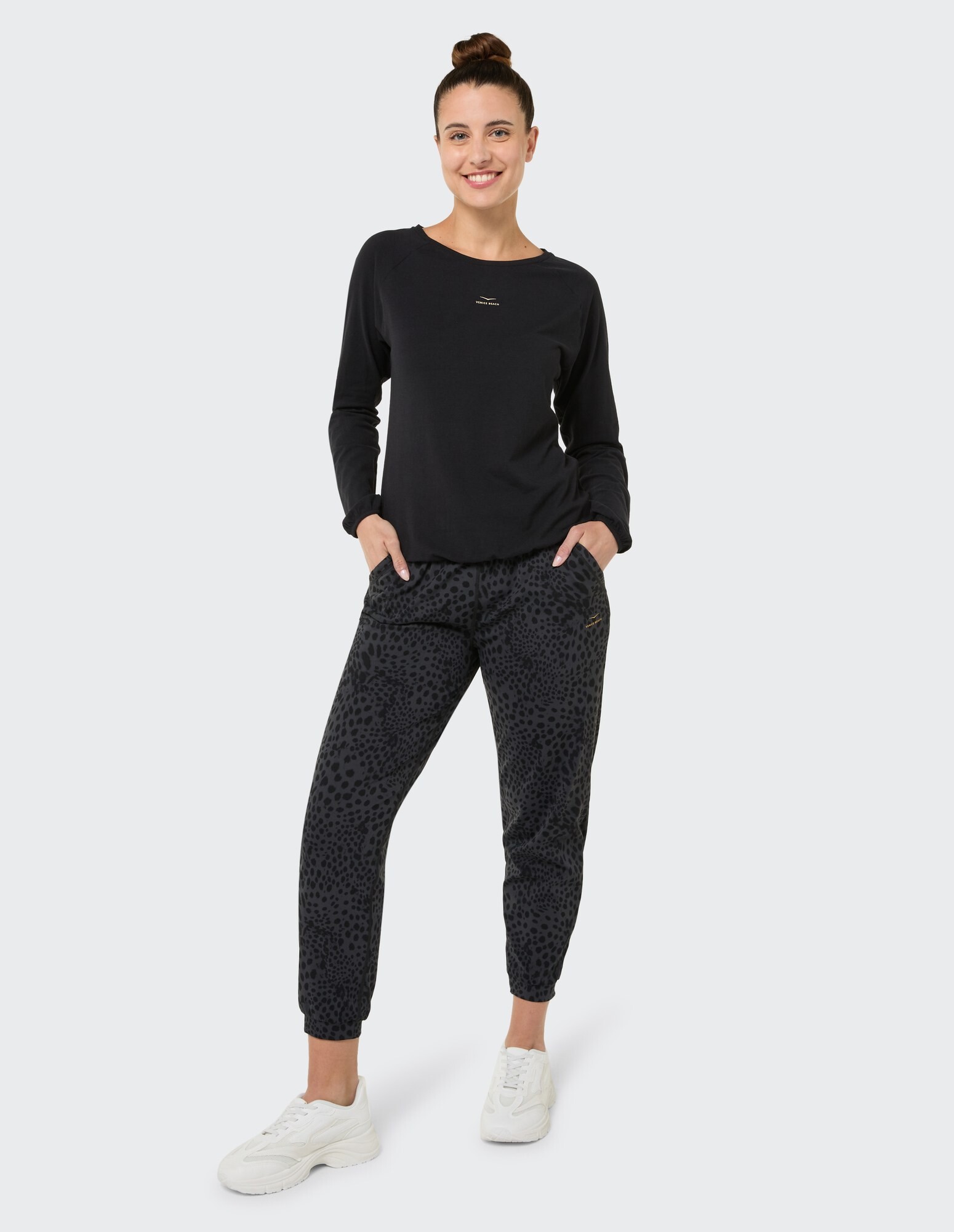 Frau in schwarzem Langarmshirt und Jogginghose mit Leopardenmuster, lächelnd.