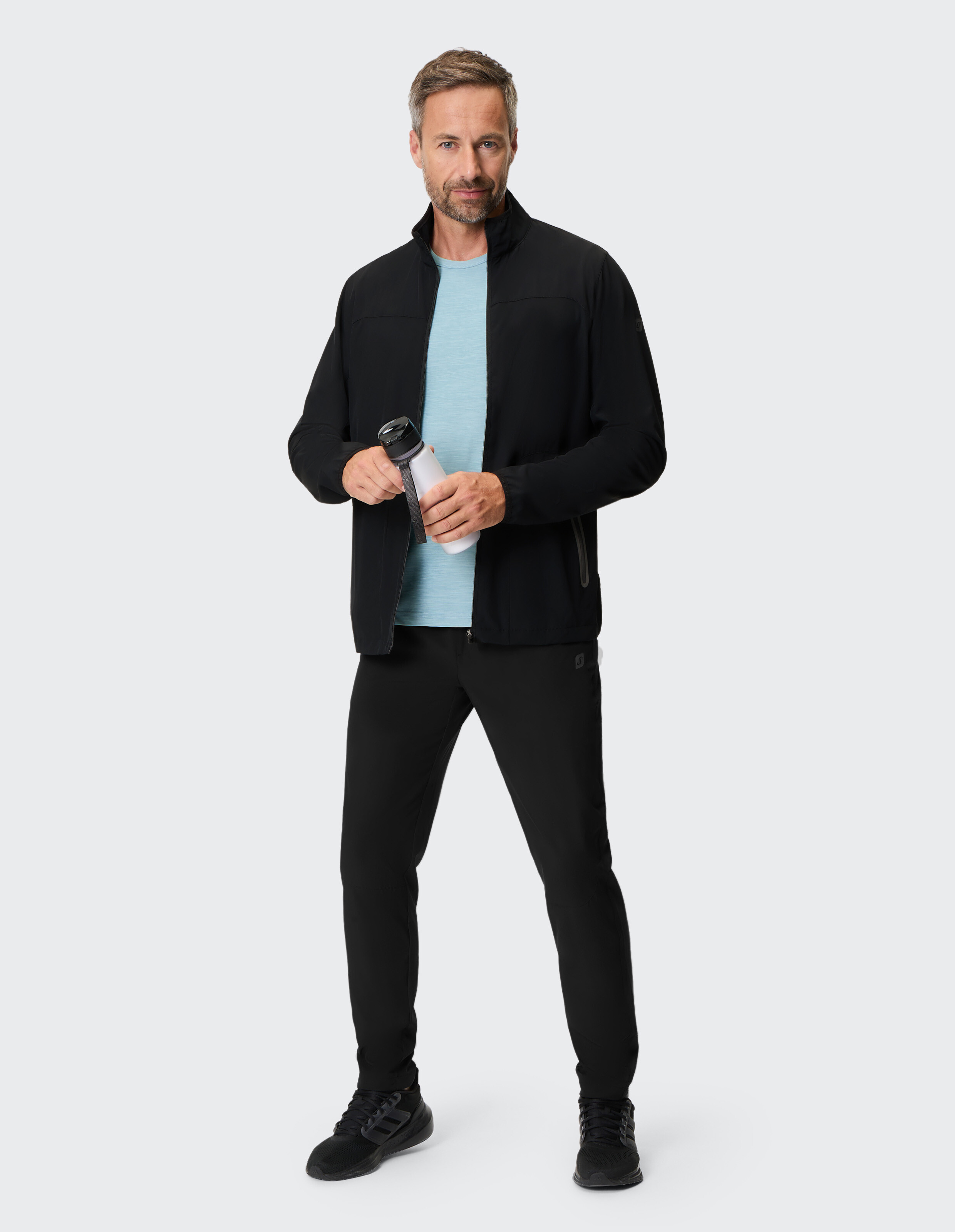 Mann trägt eine schwarze Jacke mit Reißverschluss und passende Jogginghosen für einen bequemen, lässigen Look.