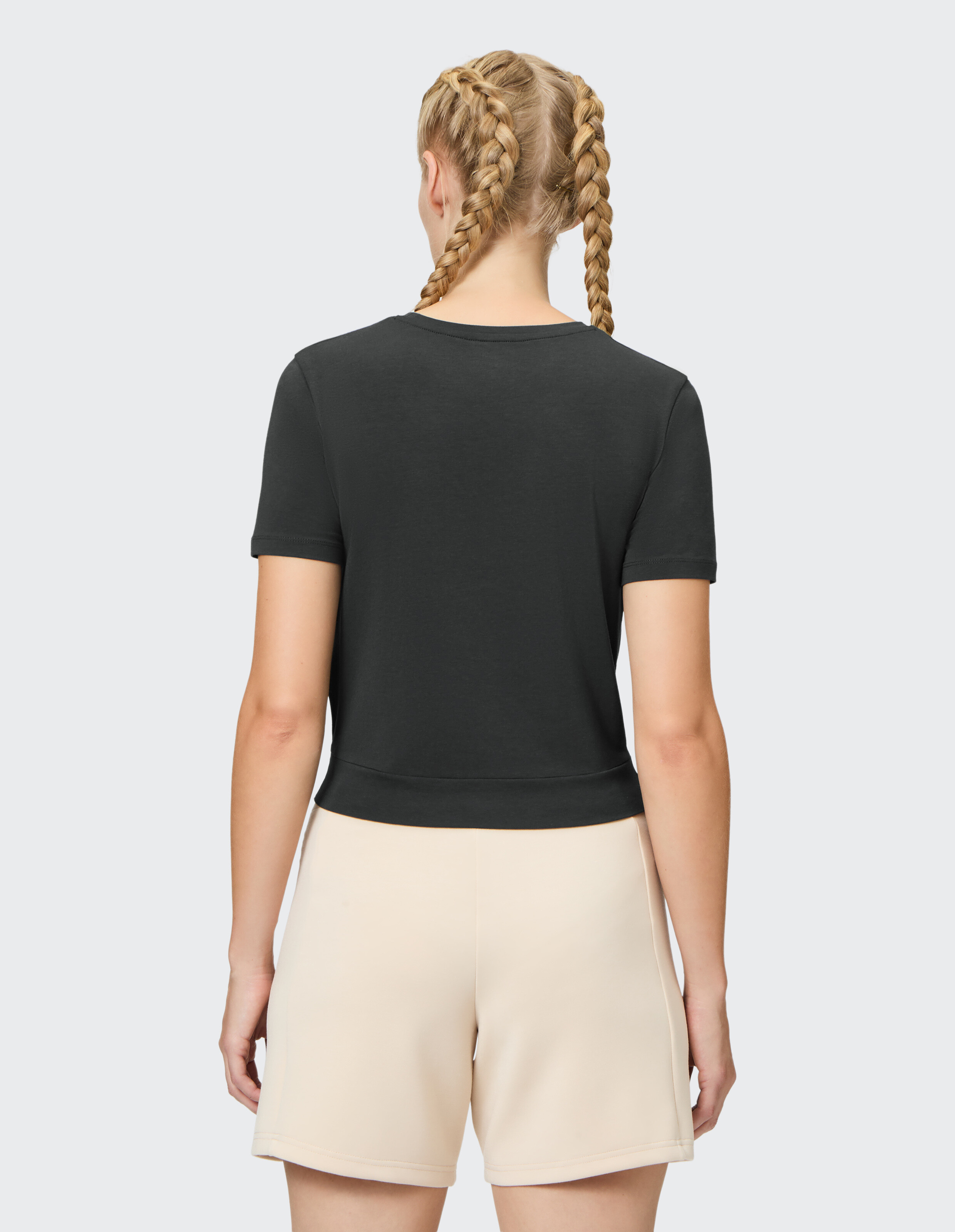 Rückansicht einer Frau, die ein schwarzes Freizeit-T-Shirt und beige Shorts trägt.