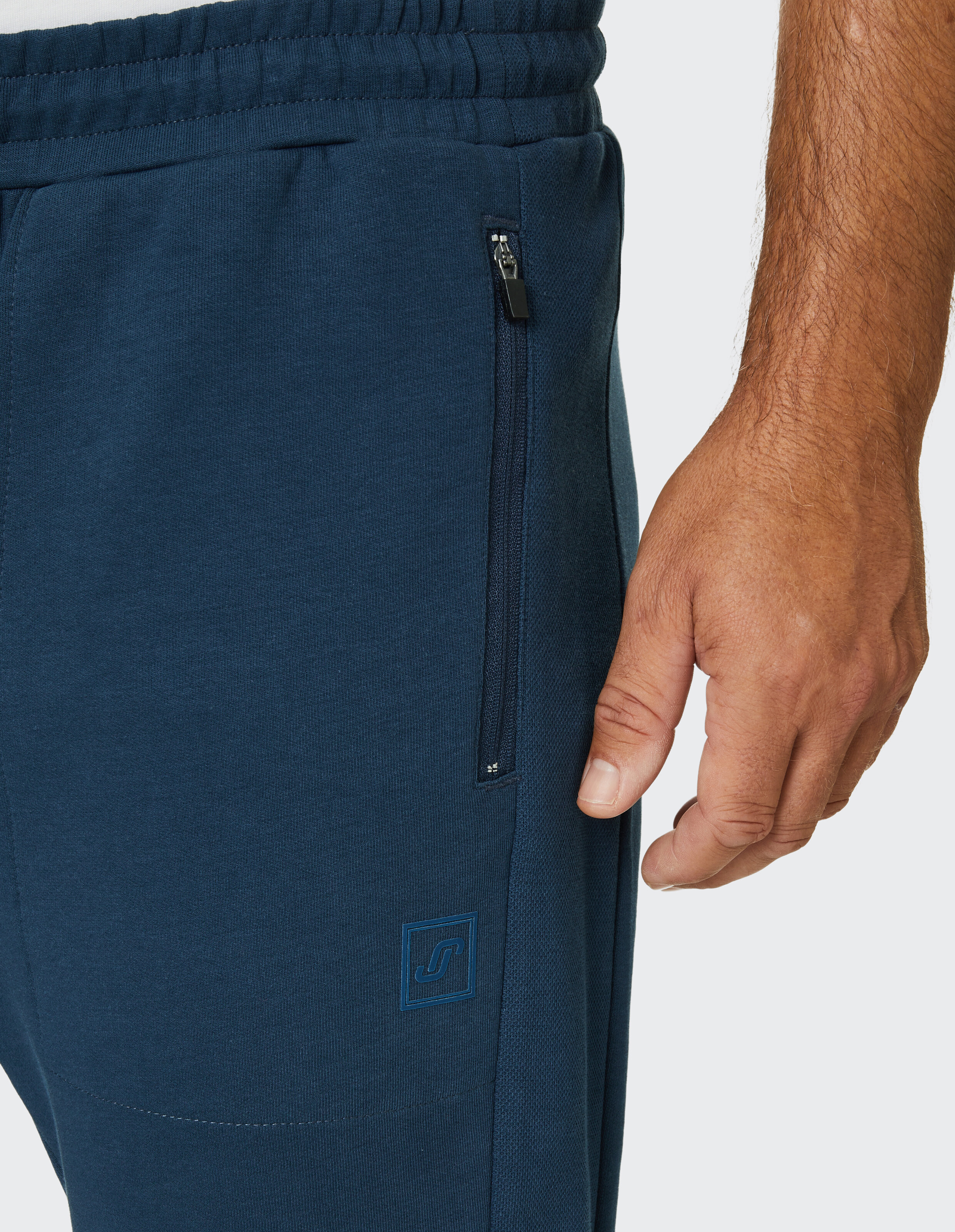 Nahaufnahme einer dunkelblauen Jogginghose mit Reißverschlusstasche, elastischem Bund und einer Hand, die neben dem Bein ruht.