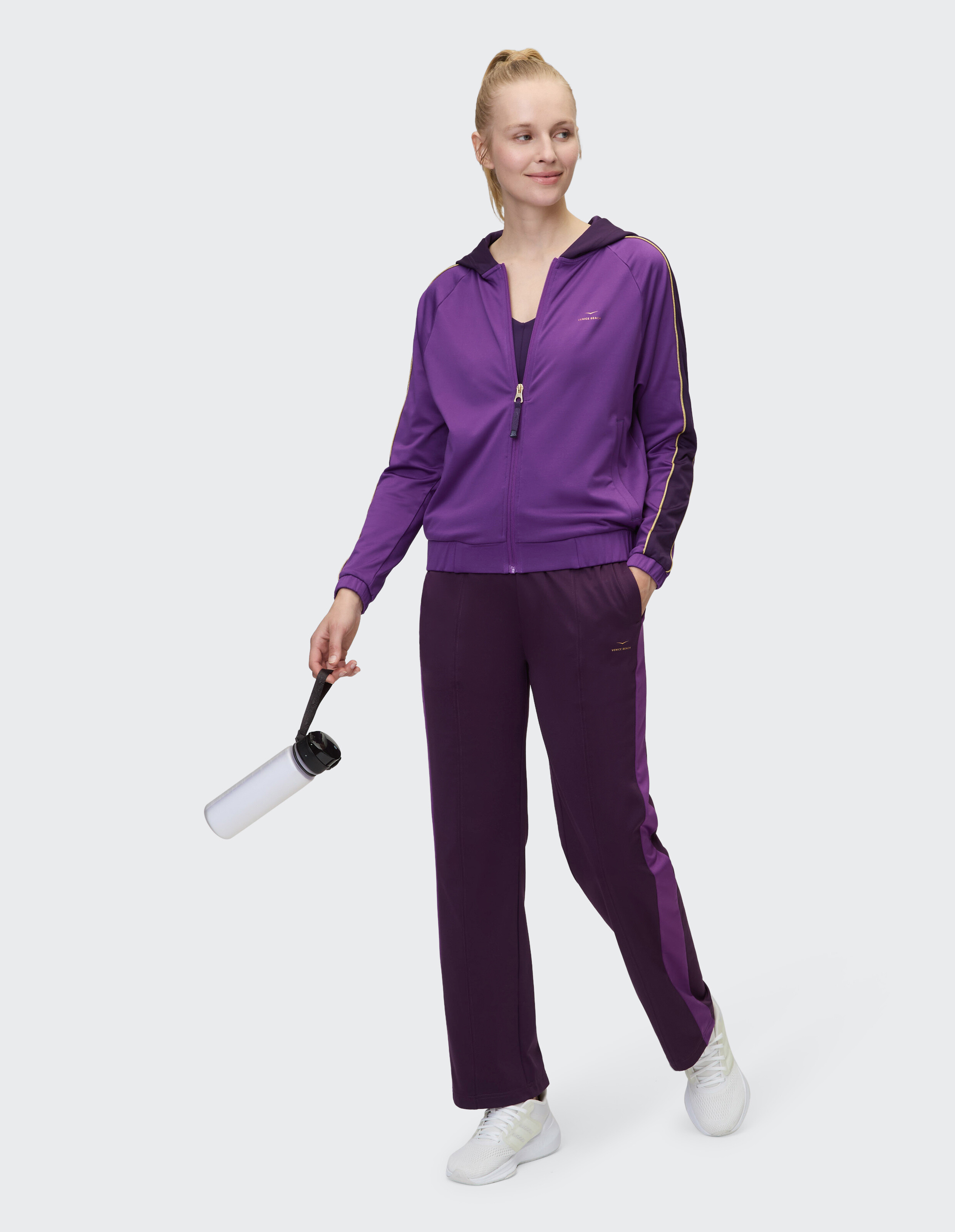 Frau trägt eine lila ELBSAND-Trainingsjacke mit Reißverschluss und eine passende Lounge-Hose.