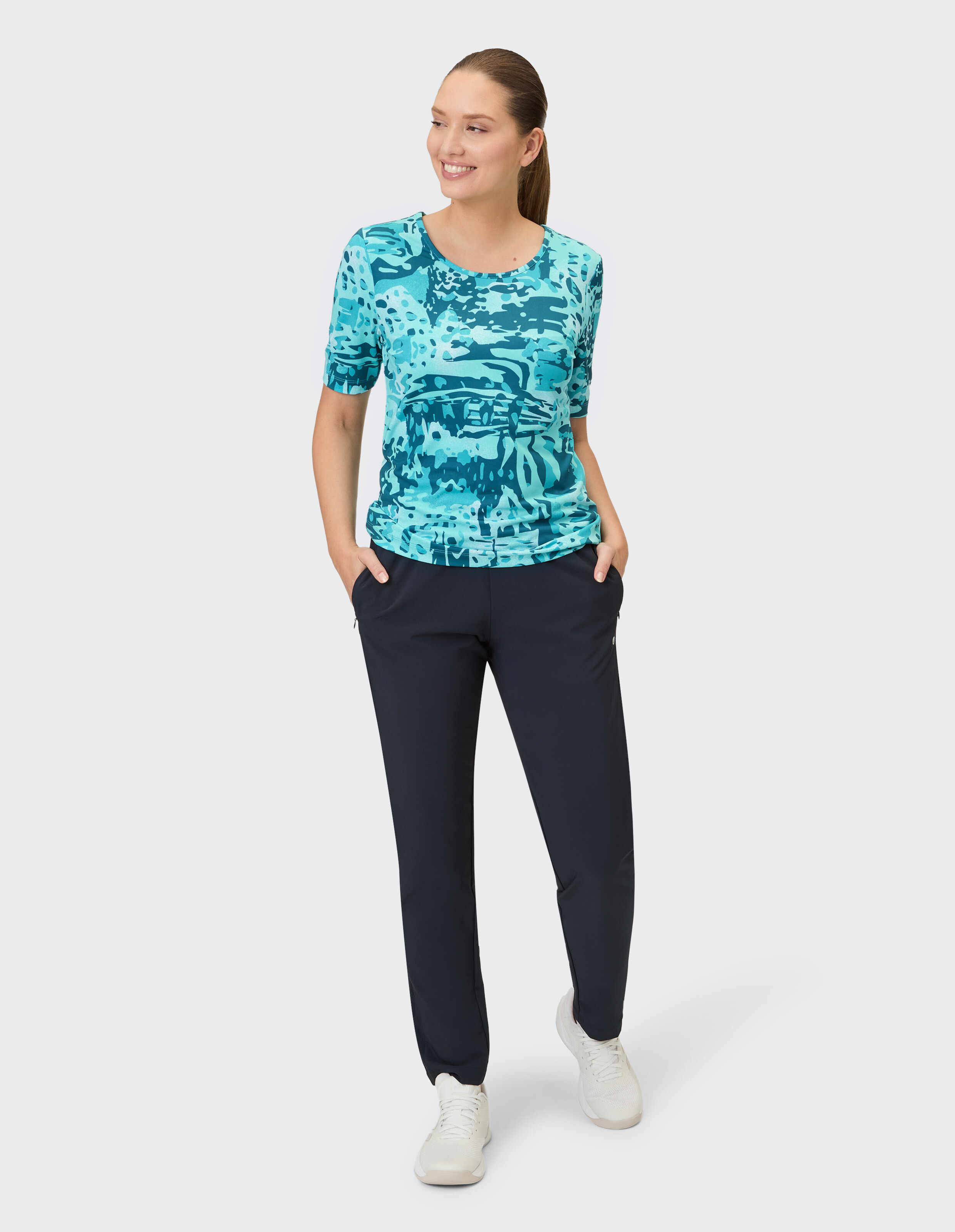 Ein Frau trägt ein blaues T-Shirt mit Camouflage-Muster und eine schwarze Hose.